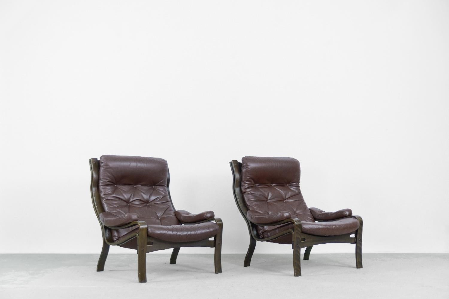 This set of high armchairs was manufactured in Scandinavia (probably Norway) during the 1970s. The solid structure is made of molded wood. The quilted pillows are upholstered with natural leather in a dark chocolate color. The armrests are