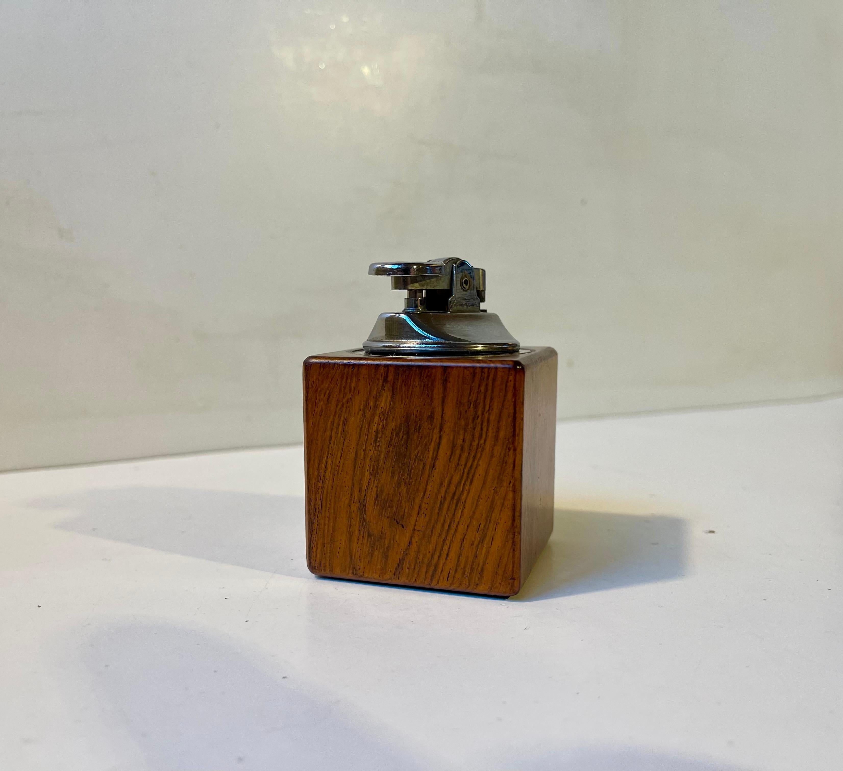 Encendedor de mesa para puros/cigarrillos de fabricación sencilla, en teca maciza y metal cromado. Fabricado en Escandinavia durante los años 60 a partir de teca sobrante de muebles. Funcionaba cuando se probó. Medidas: 7,5 cm. D/W: 5 cm.