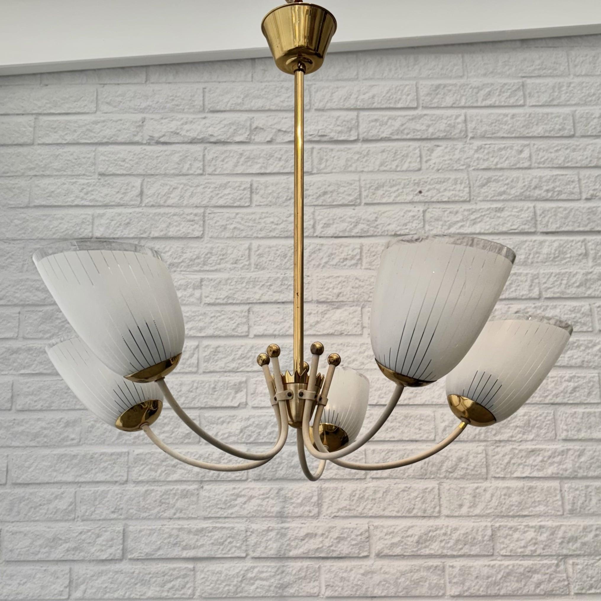 A beautiful vintage chandelier crafted from brass, featuring five curved arms that hold bell-shaped glass shades. The arms are anchored by a decorative solid brass crown, with each arm adorned with a brass ball. A matching brass canopy is fitted