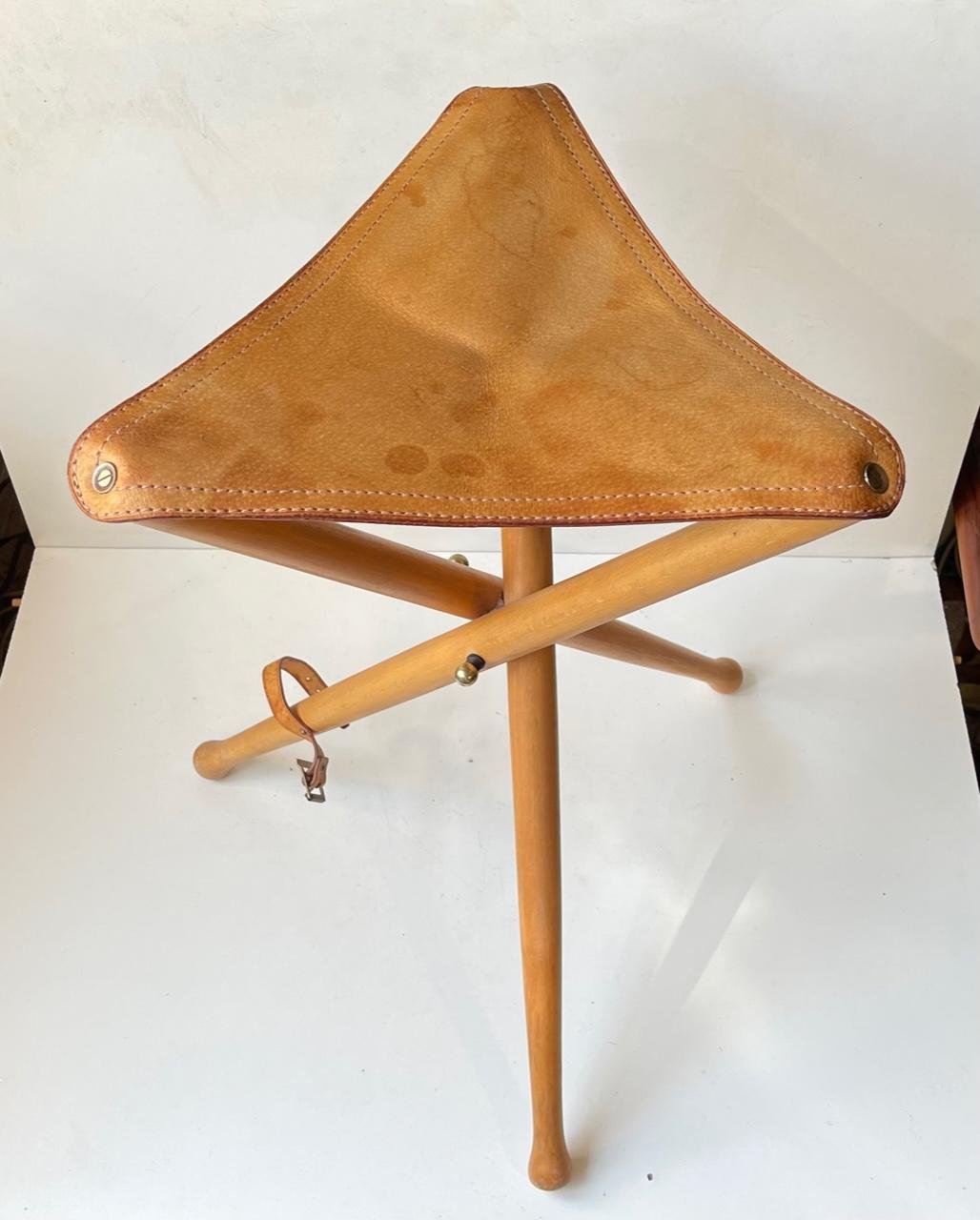 Tabouret de chasse vintage scandinave tripode avec des pieds en bois de hêtre massif laqué et une assise en cuir de selle tanné épais. Fabriqué dans les années 1960 ou 1970. Dimensions : H : 52 cm, L/D : 35/31 cm debout.