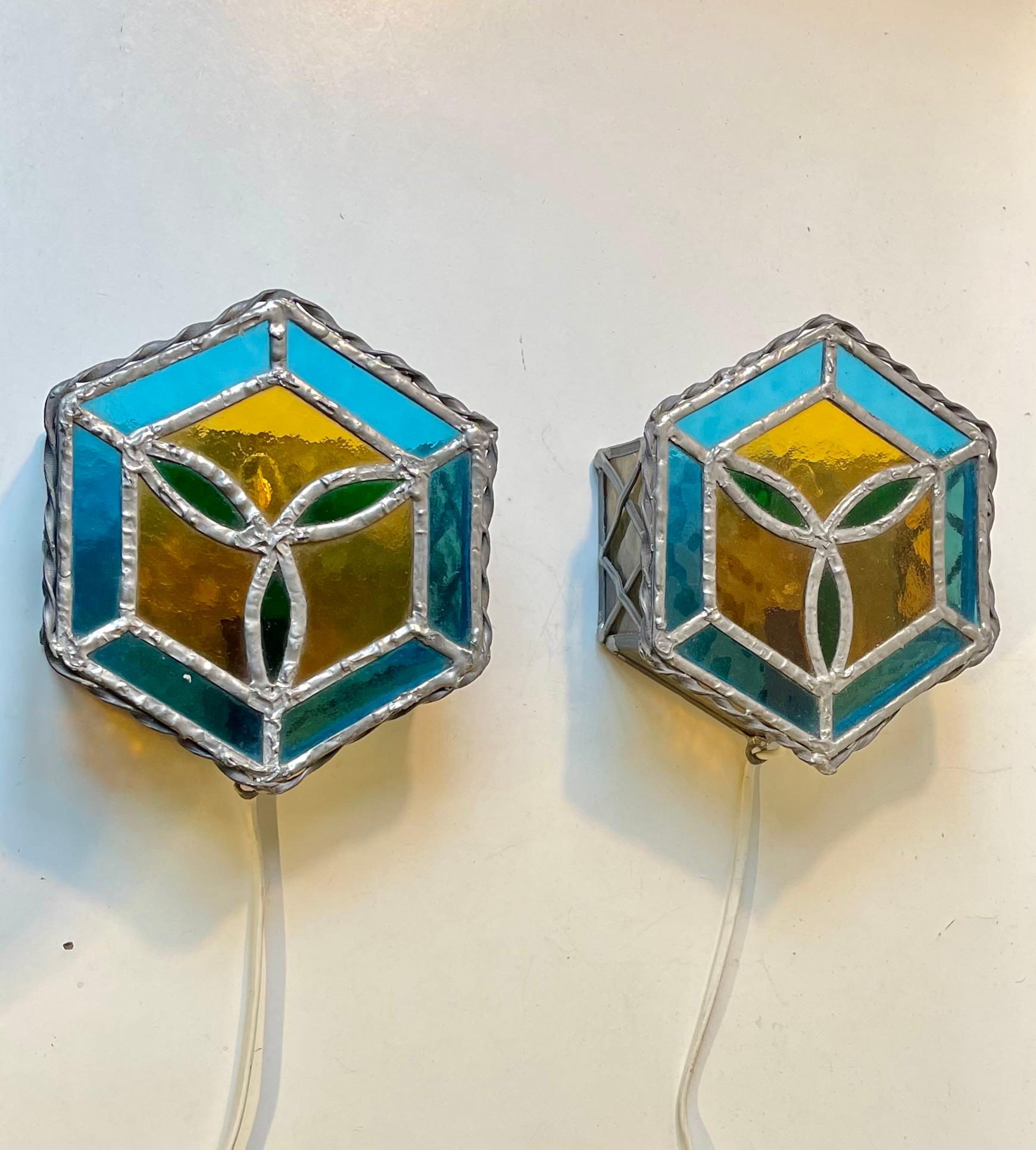 A pair of hexagonal stained glass wall lamps with green, blue and yellow panelling. Gothic revival in style and handmade in Scandinavia during the 1970s. They are installed with E14 28 watts sockets/bulbs. Measurements: 20x18x7,5 cm. Both in working