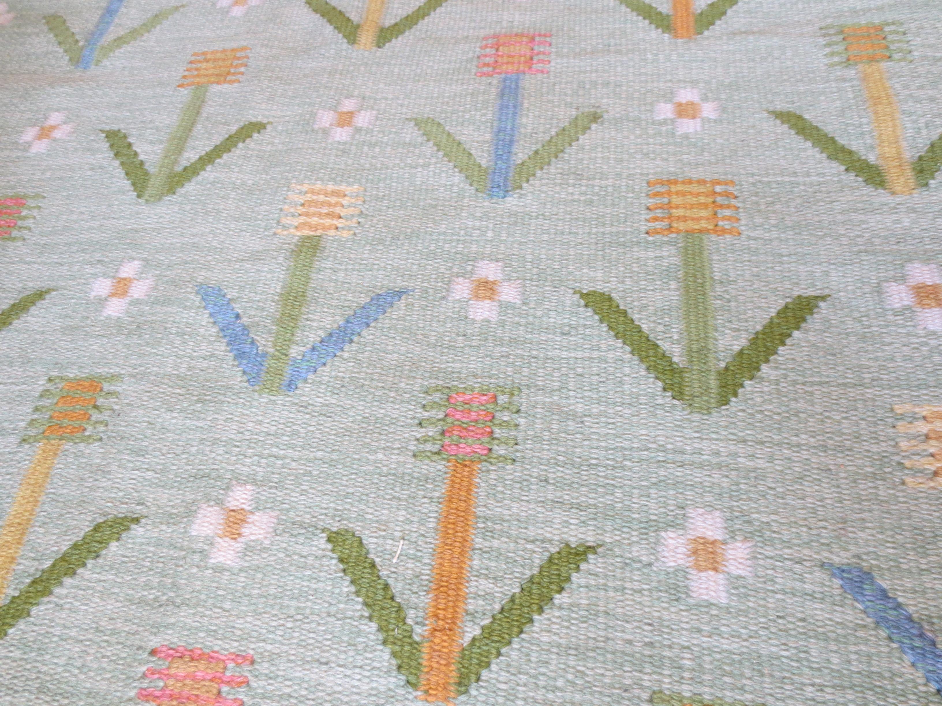 This is a vintage Scandinavian Kilim rug, woven circa 1950s, comprising of an all-over geometric floral pattern on a green backdrop anchored with a border. It is Minimalist in design, but yet beautifully intermingled with a soft color palette. The