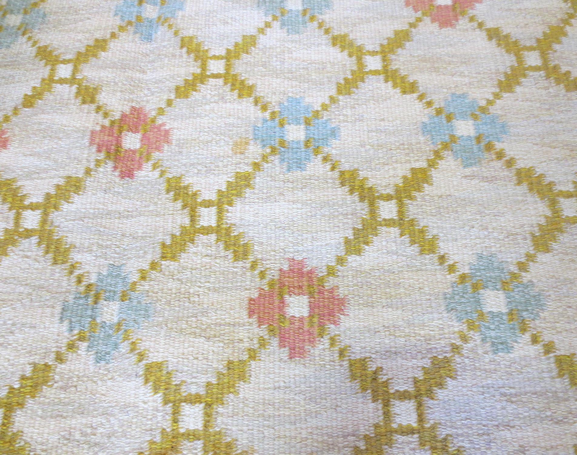 This is a vintage Scandinavian Kilim from the mid-20th century. It features dainty geometric florals rendered in a lattice work pattern of soft blues, pinks, and yellow greens which is set on an ivory background. This Minimalist yet beautiful