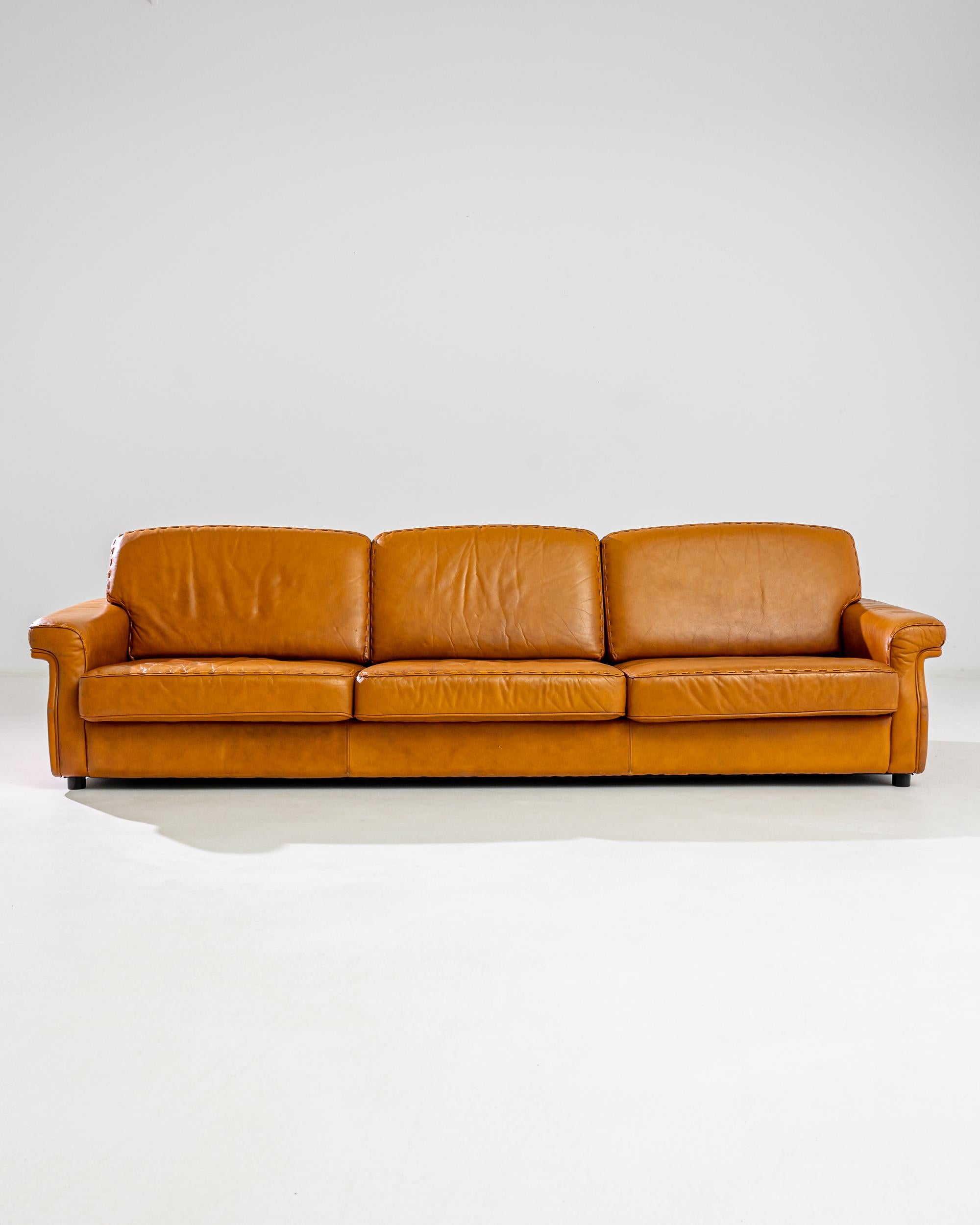 Made in Scandinavia, this vintage three-seater sofa features comfortable wide cushions and curved armrests held up by a sturdy base. The intense tawny hue of the high quality leather upholstery exudes warmth and coziness accentuated by the