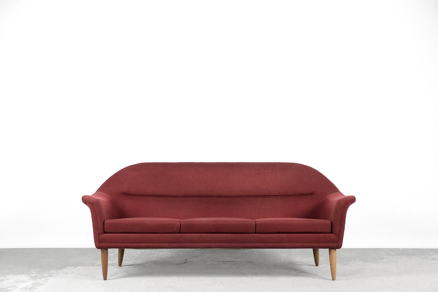 Este sofá de tres plazas fue fabricado por el fabricante sueco Bröderna Anderssons en la década de 1950. El sofá está tapizado con un material de alta calidad en un noble color rojo. Es un ejemplo de una antigua escuela artesanal, en la que el