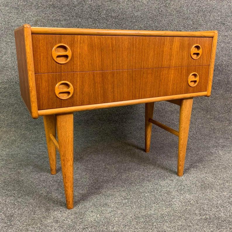 Here is a small 1960s entry chest in teak wood recently imported from Denmark to California.
This case good features a vibrant teak wood grain, a set of two dove tail built drawers with carved handles and a set of four tapered legs with stretchers.