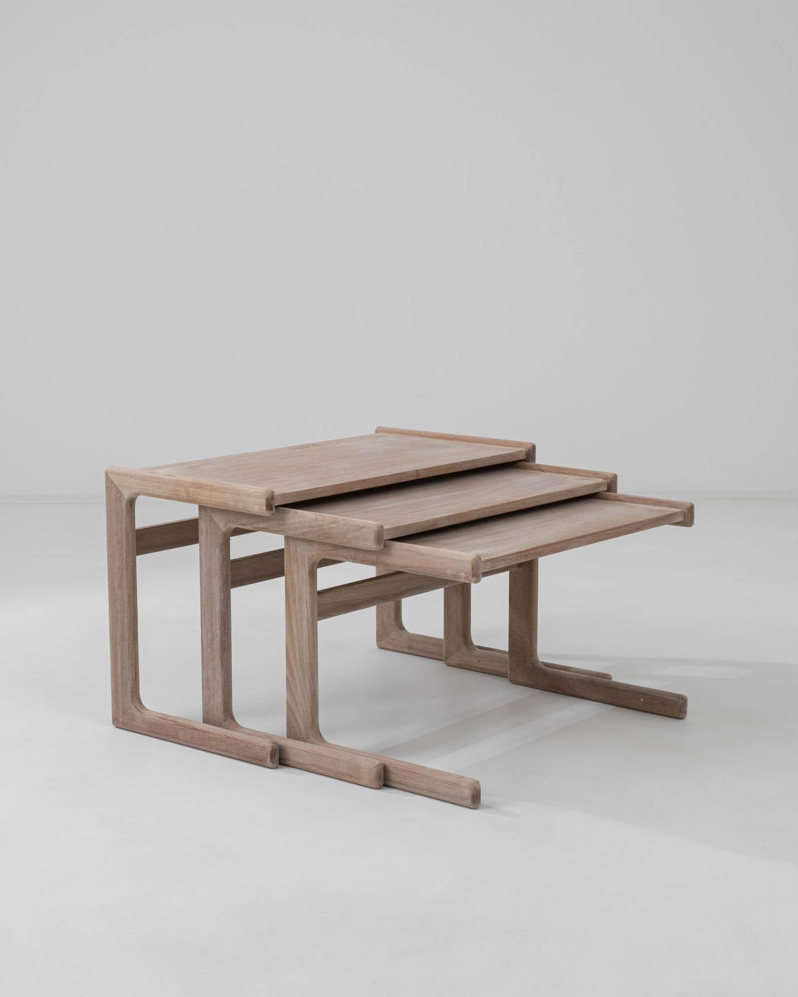 This set of teak nesting tables was designed in Denmark in the 1970s. Dynamically composed with traditional materials and quality construction, the design bears the stamp of Scandinavian Modernism. Slender, linear table legs support a tray-like