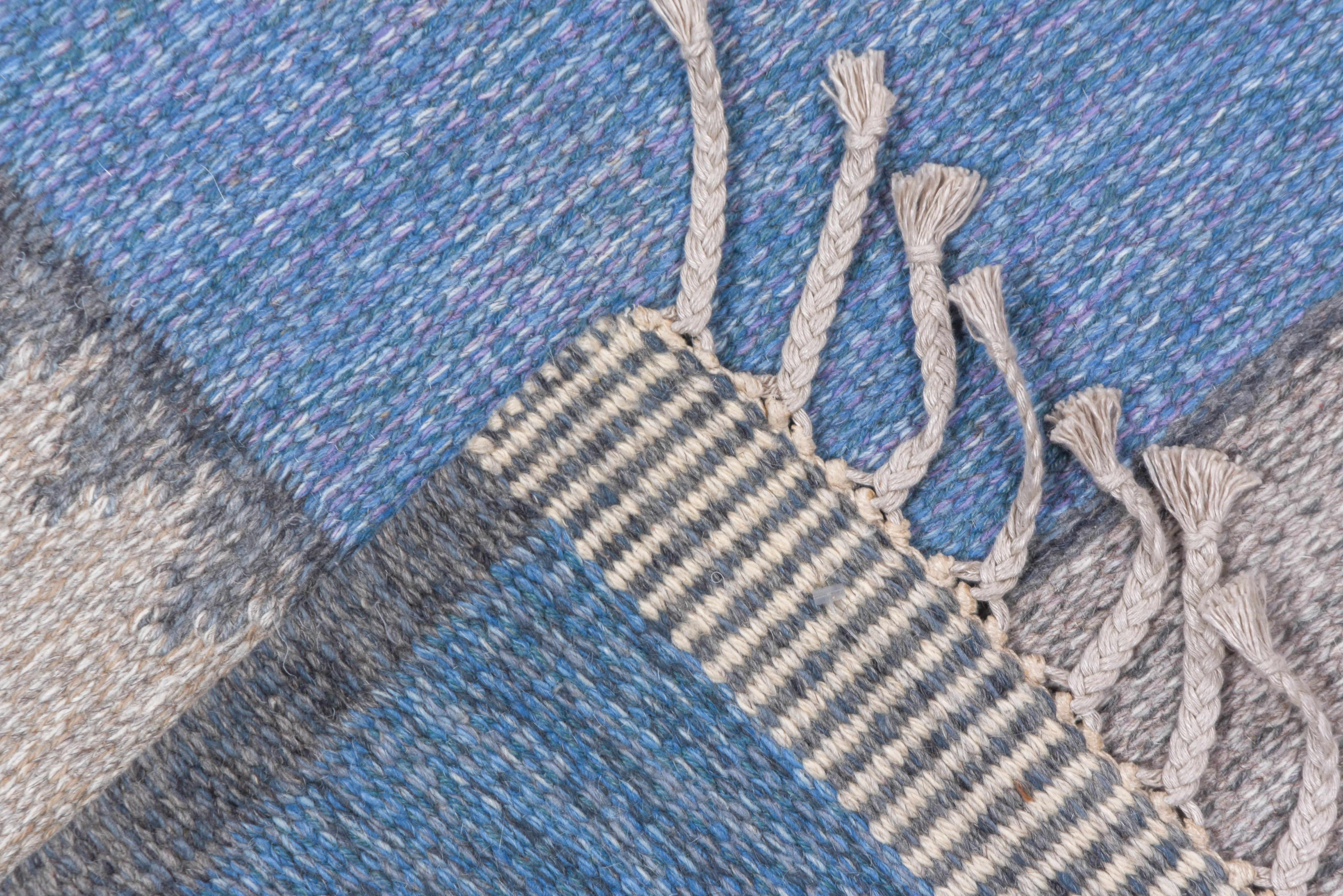 A plain, slightly varied, light blue field is framed by a border of squares in shades of light blue, pale blue, and light grey, with cross details in every second panel. Wool pattern weft, tapestry weave. End finish tassels. A picture frame without