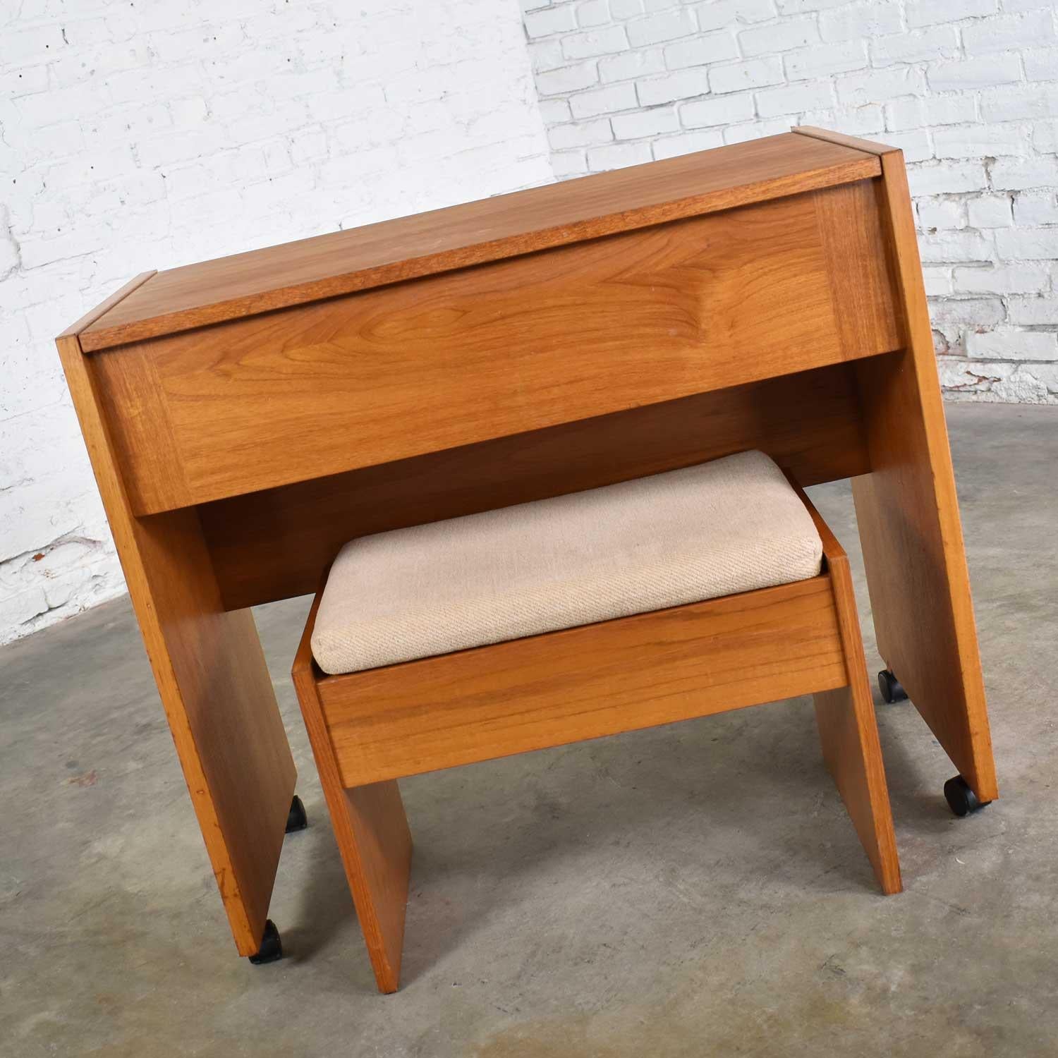 Awesome Scandinavian Modern rolling make up vanity and bench in teak with flip open mirror and storage. It is in wonderful vintage condition. The finish has been restored and given a coat of poly. It has no outstanding flaws that we have found but