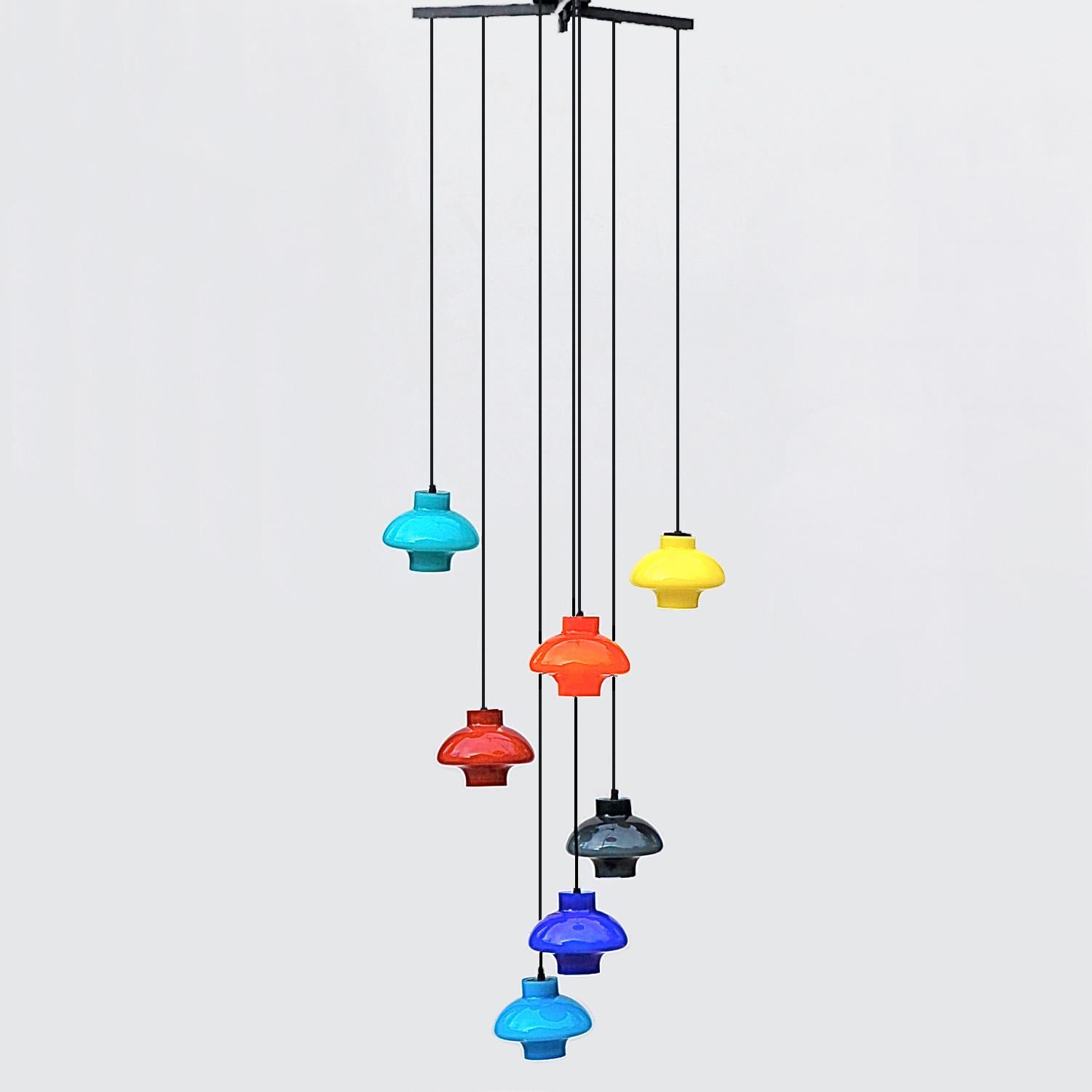 Scandinavian, 1960s cluster or cascade pendant light with staggered, multicolored lamp shades suspended from a metal tripod frame (flush mount). There are seven shades in bold colors: blue, green, black, yellow, orange and red. The multicolored