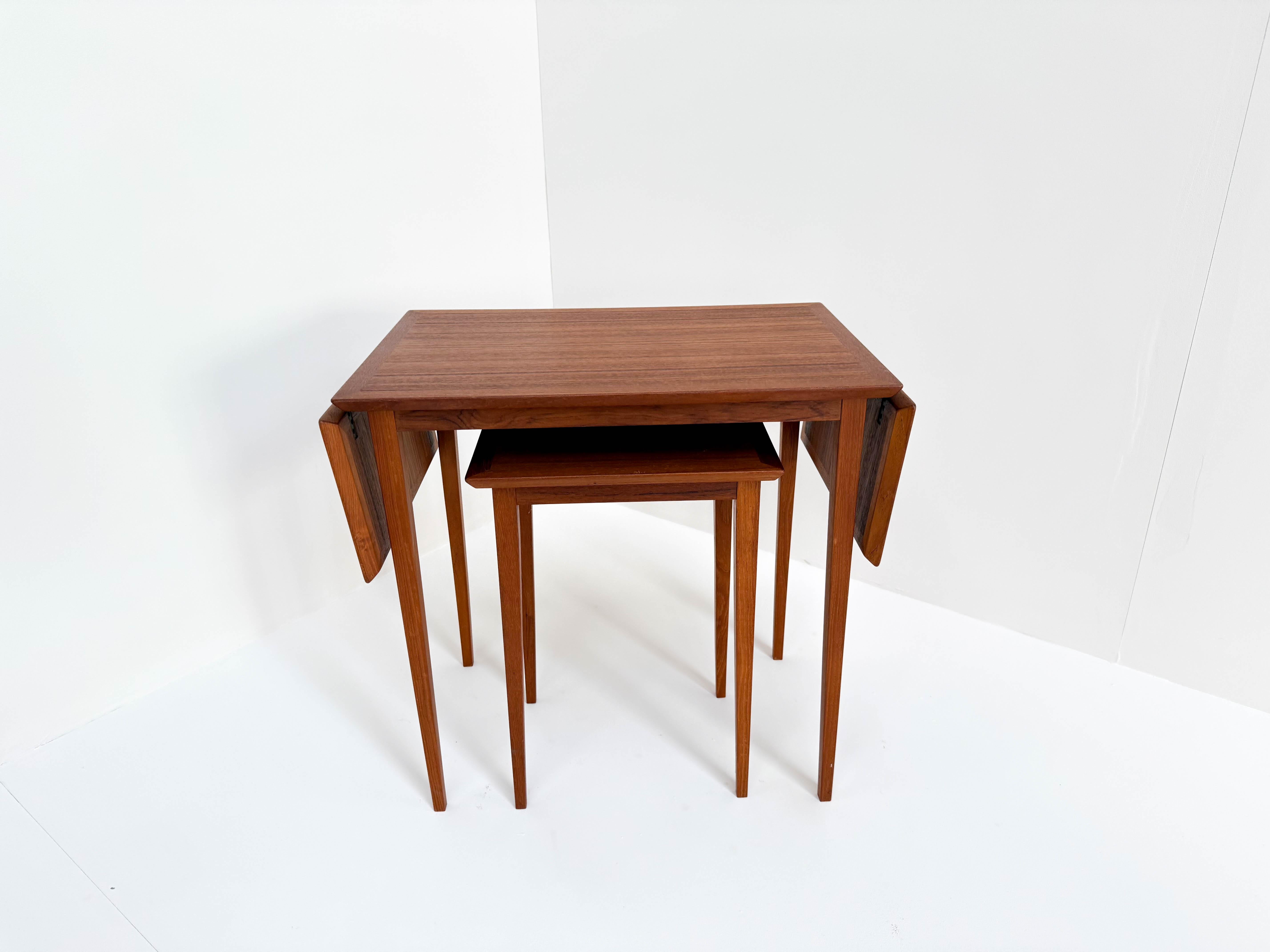 This is a beautiful vintage Scandinavian nesting table set made of warm-toned wood. The design is practical and stylish, featuring a larger table with two foldable side panels and a smaller nesting table that fits neatly underneath. When closed, the