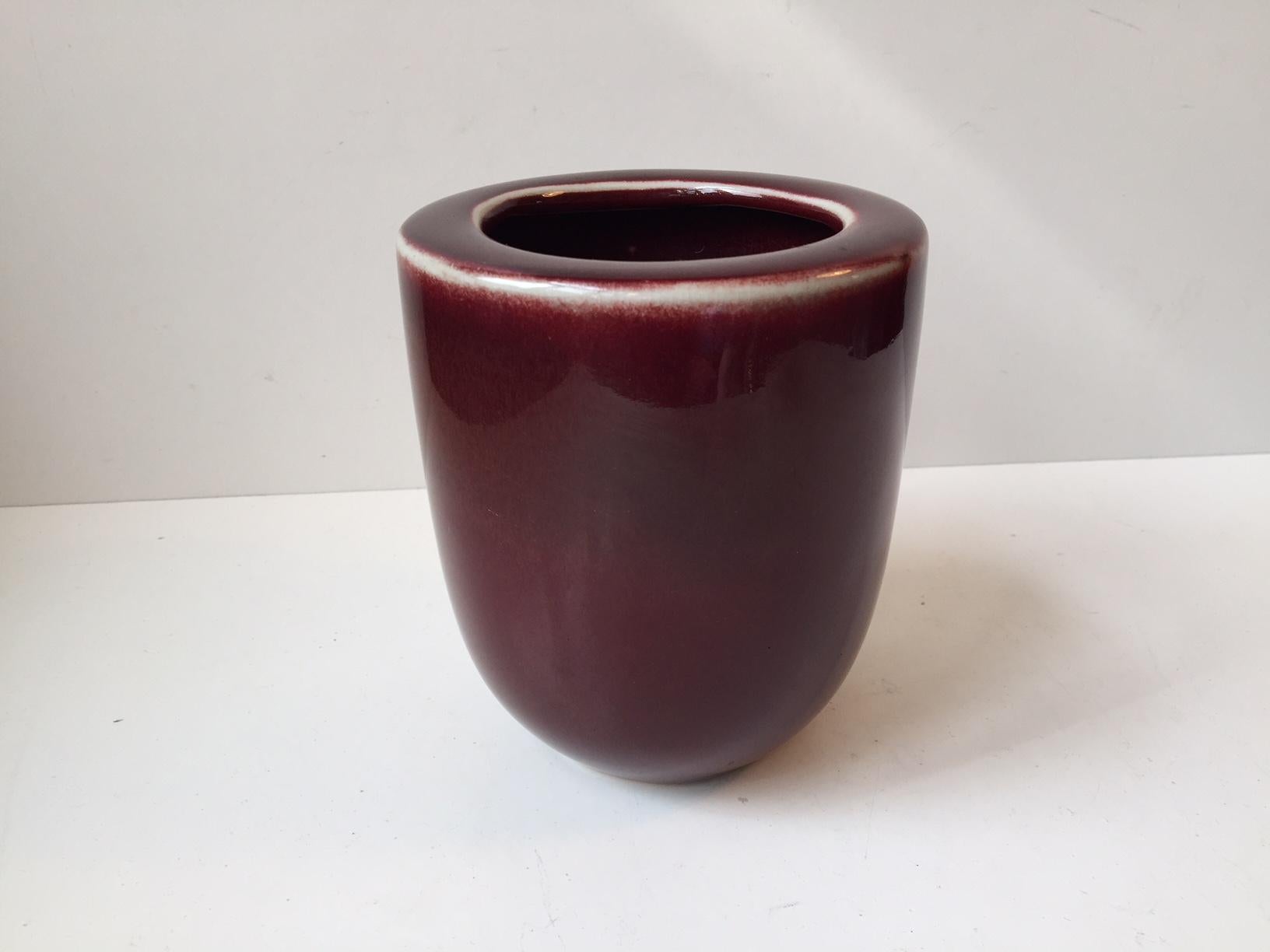 This vase in the style of Nils Thorsson and Daniel Andersen is made of ceramic glazed in oxblood red, highlighted by white edges.