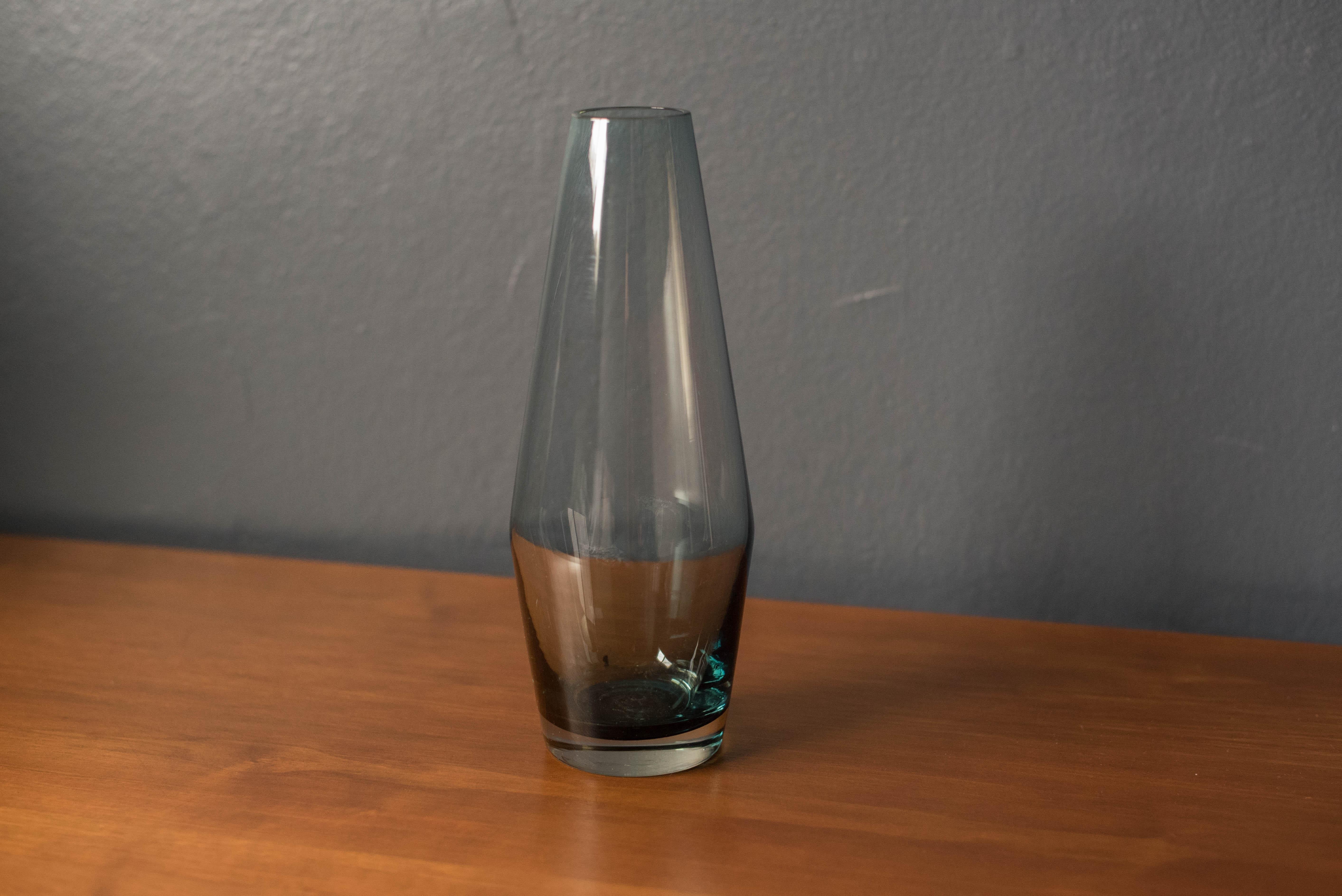 Mid-Century Modern glass bud vase by Riihimaki, Riihimaen Lasi Oy, Finland. This decorative piece has a smokey blue tint with a smooth surface finish.