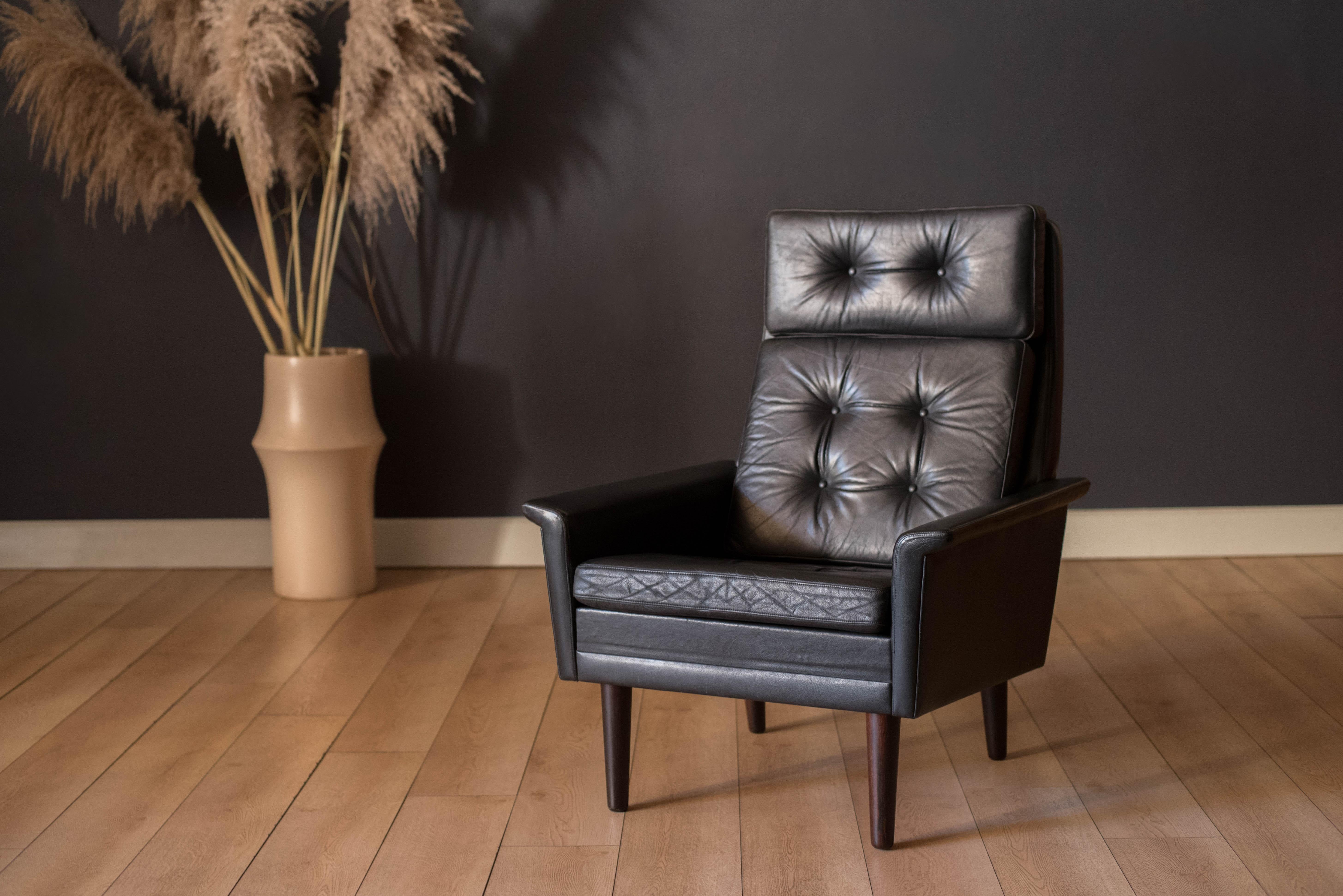 Mid century modern highback lounge chair in rosewood and leather circa 1960's, Denmark. Features the original patinated black leather and sculptural curved armrests supported by rosewood angled tapered legs. This relaxing lounge chair includes three