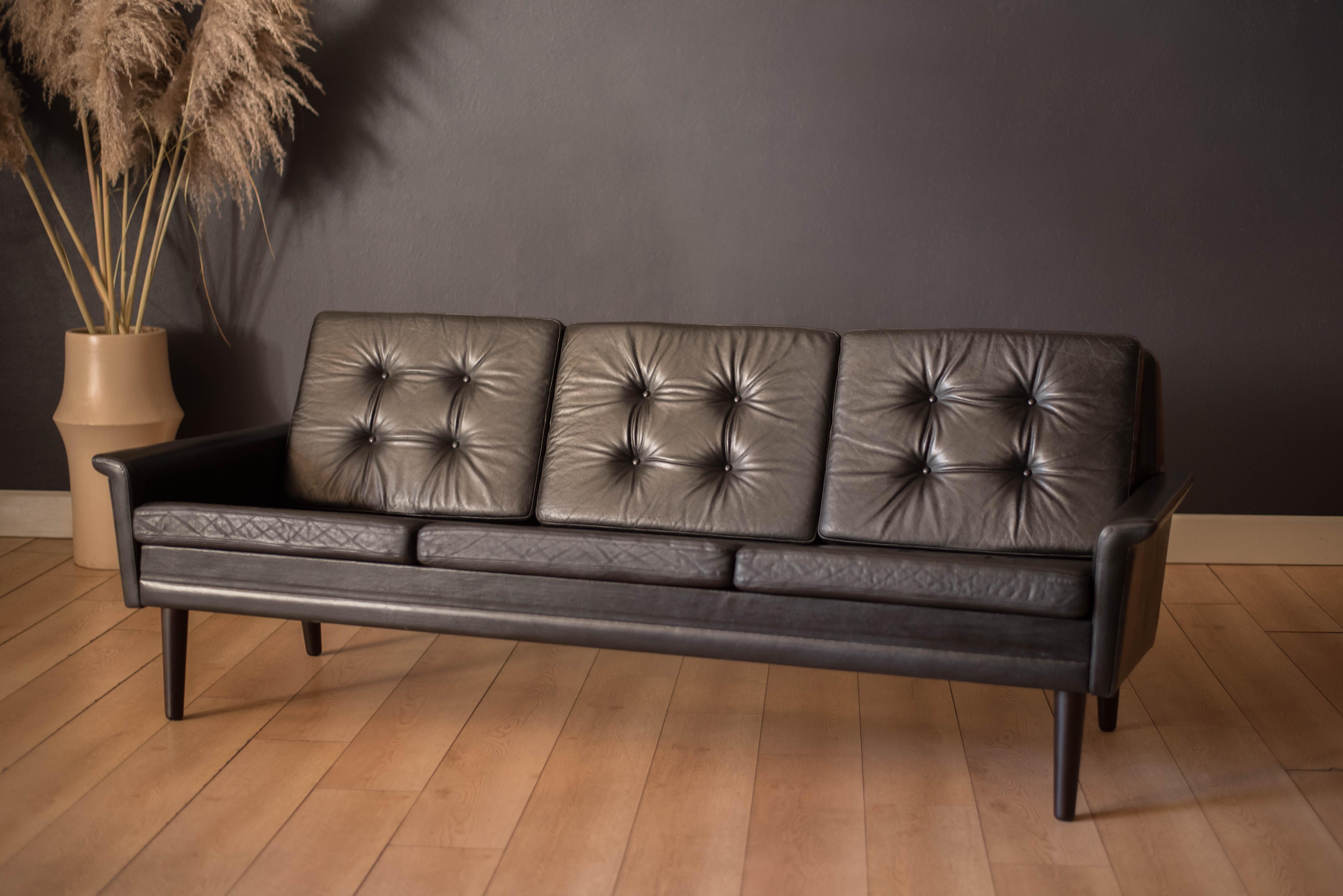 Mid century modern 3-seater sofa in rosewood and leather circa 1960's, Denmark. This comfortable statement piece can be displayed from any angle and features sculptural curved armrests. Retains the original patinated black leather designed with