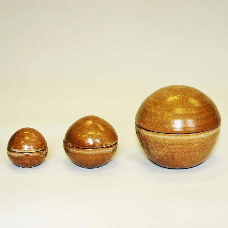 Lovely vintage set of three ceramic lid boxes/caskets from Scandinavia  around 1970s. These three casket have a top and a bottom and shaped as round lozenges. Divided in the middle in two seperate and equal parts. Brown rustic glazed earth colors in