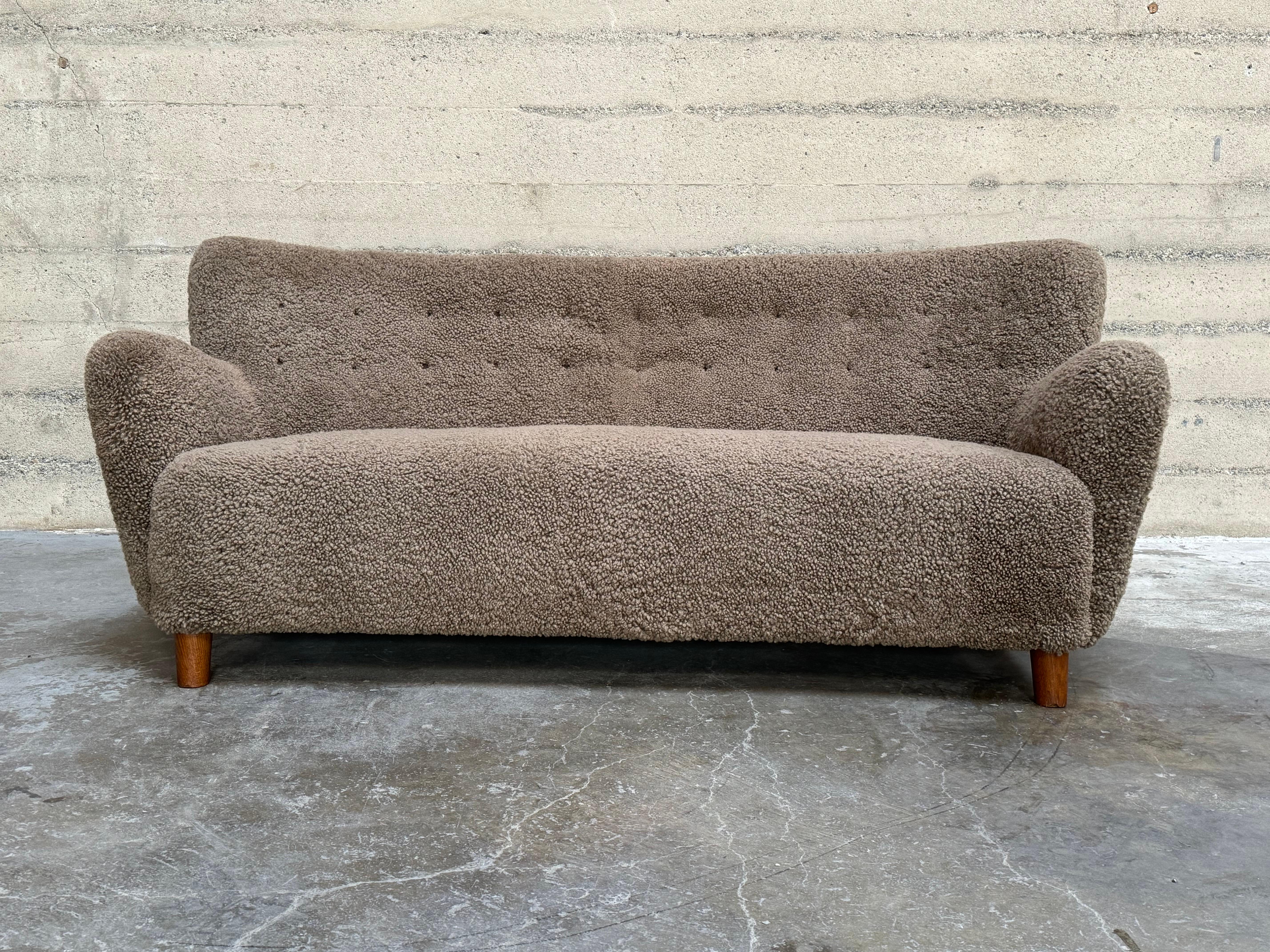 Freshly reupholstered in a mushroom-toned sheepskin. Circa 1930s-40s cabinetmaker sofa imported from Denmark. Stunning. Having an attractively curved shape to the arms and back off set by the chunky sweptback legs.