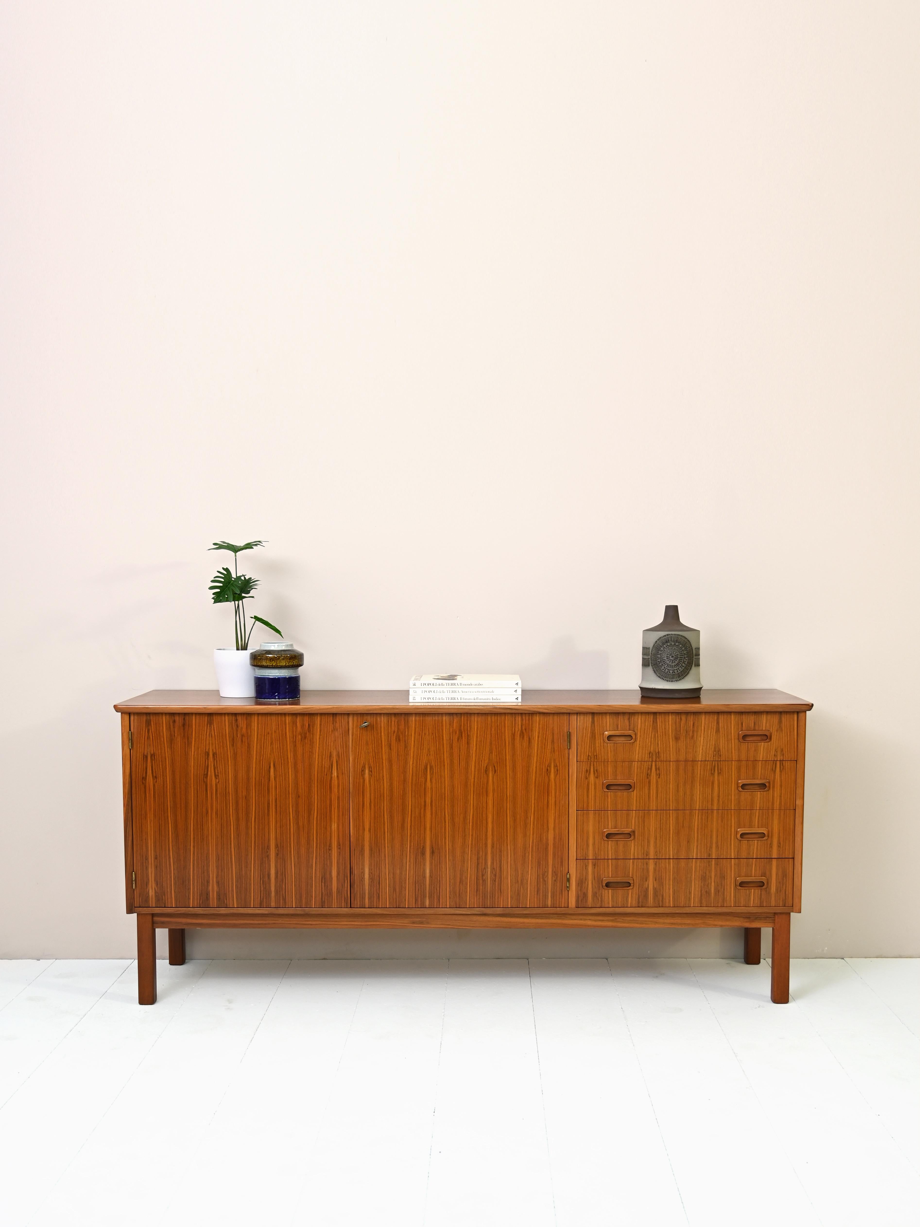Sideboard cabinet of Scandinavian manufacture from the 1960s.

This teak wood sideboard features a simple, linear shape. The two hinged doors
conceal a large storage compartment equipped with shelving.
Attention to detail is evident in the