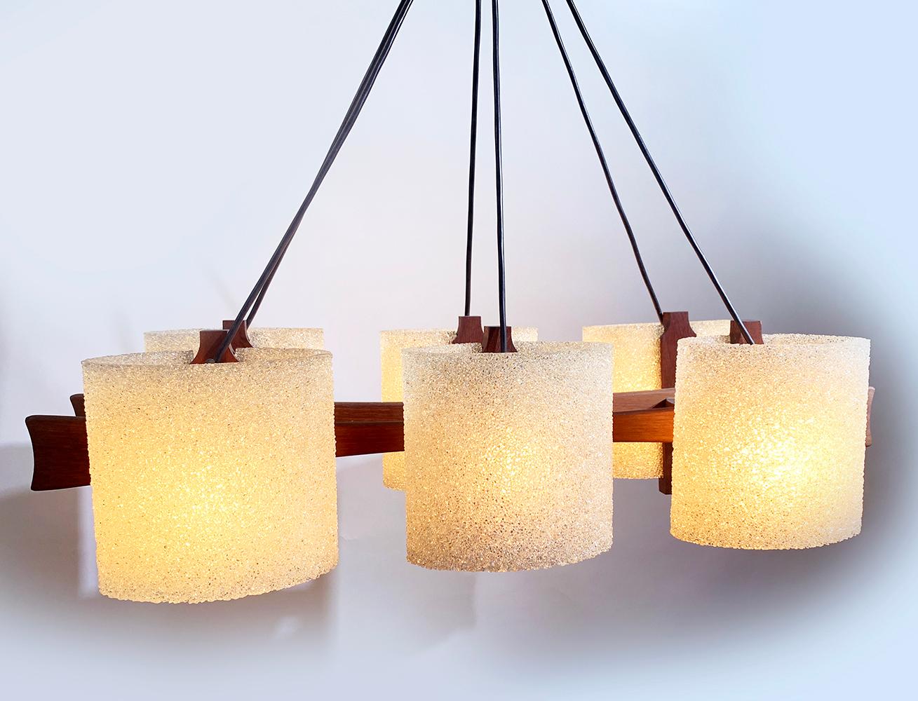 Here's a vintage 6-tulips chandelier with it's soft light that gives a really warm atmosphere.
This Scandinavian suspension from the 60s have a structure in solid teak and the 6 tulips in Perspex agglomerated resin.
It is suspended by six black