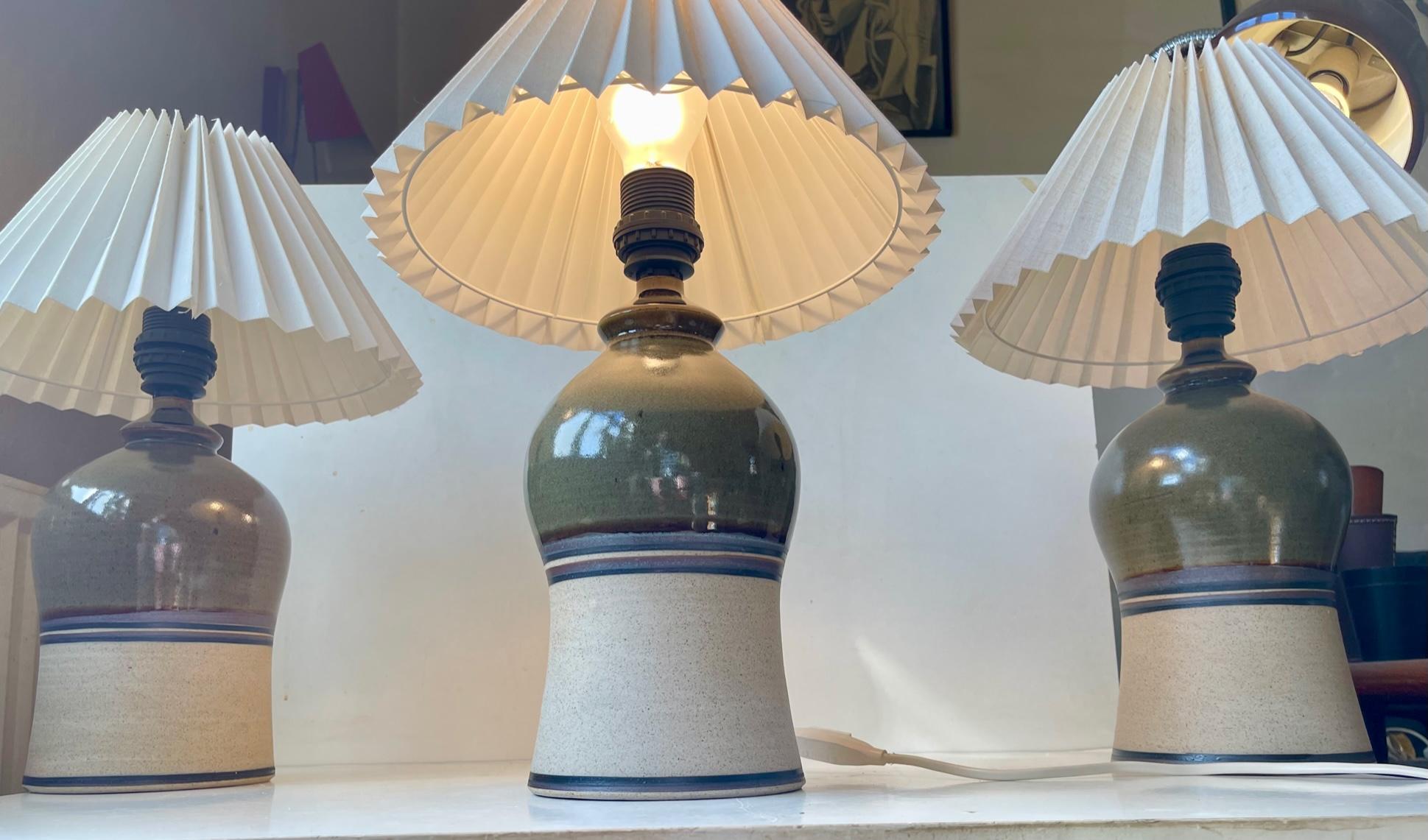 Matching set of 3 large stoneware table lights with white fluted Danish shades. Olive green main glazed highlighted with blue and earthy stripes. Studio-made by Hanne Bertelsenm in Denmark circa 1990 in the style of Tue Poulsen and Søholm.