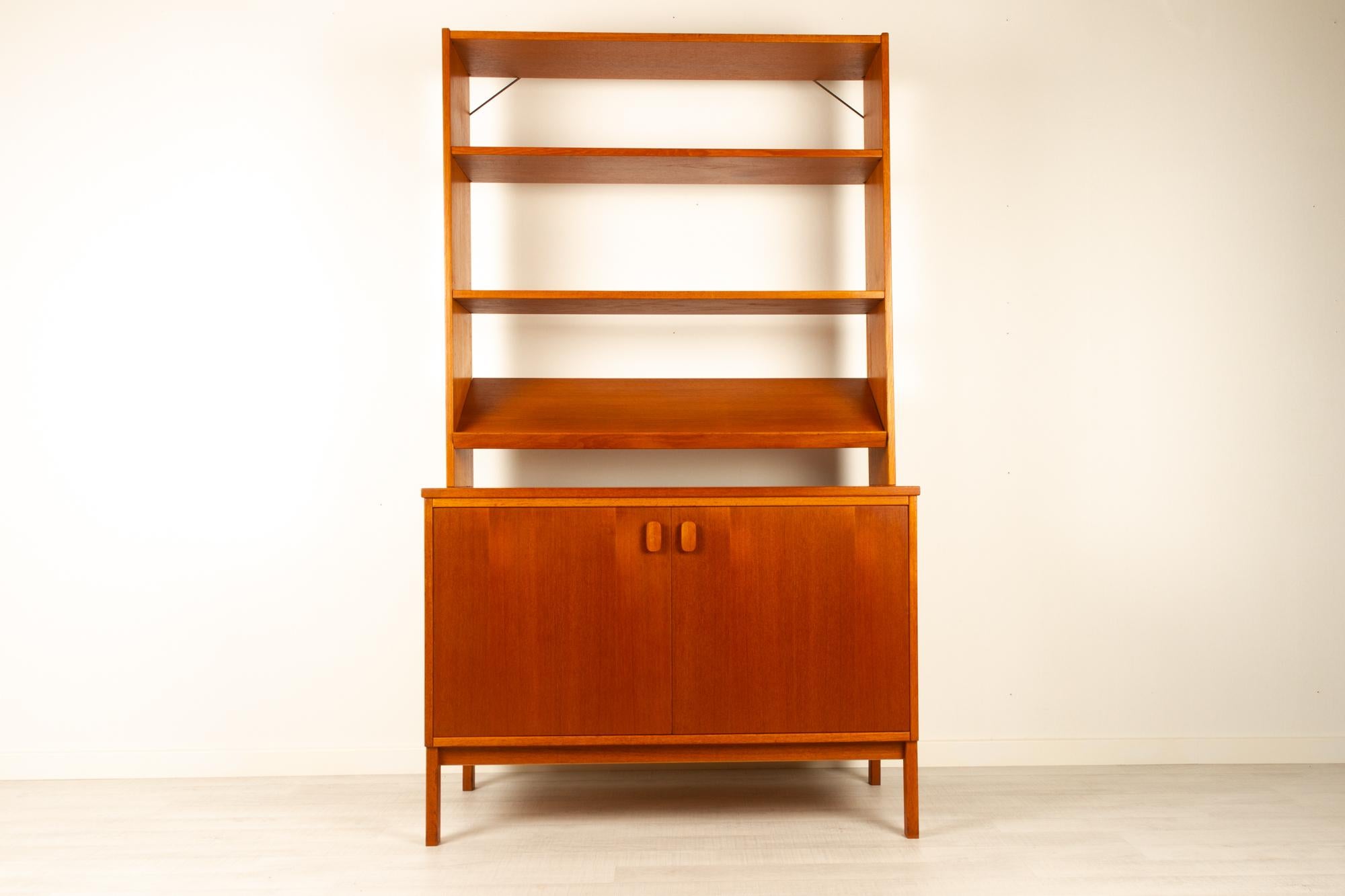 Vintage Scandinavian teak bookcase by Ulferts, 1960s
Mid-Century Modern wall unit with open shelves, made in Sweden. Four square legs in solid teak. Top section with slanted magazine shelf and open shelves. Bottom section with large cabinet with