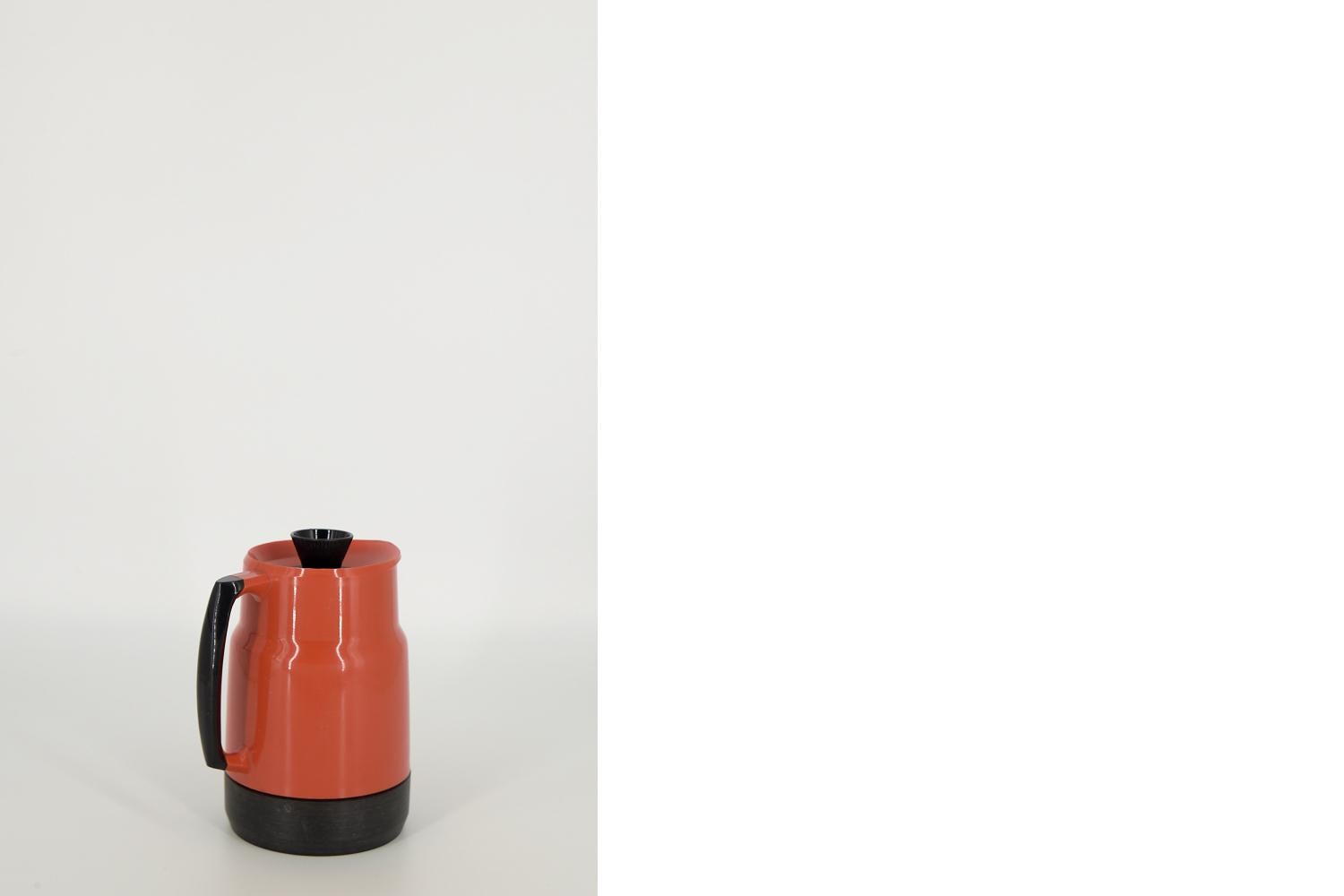 Cette petite cruche thermique a été conçue par Sigvard Bernadotte pour la manufacture suédoise Husqvarna Borstfabrik dans les années 1960. Le thermos est en plastique rouge-orange. La poignée, le couvercle et le fond sont noirs. L'entrée est conçue