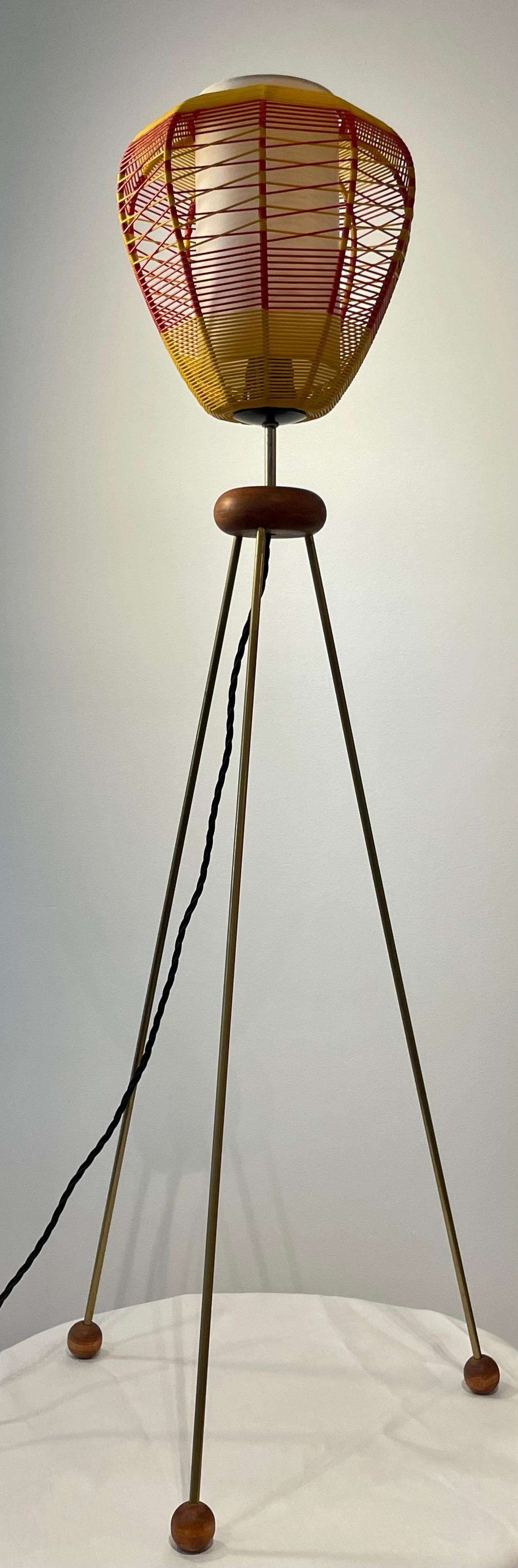 1950's Italian tripod lamp with whimsical red and yellow woven plastic shade encasing the light bulb. The metal legs form a tripod shape finished with ball feet for stability and Italian styling. 