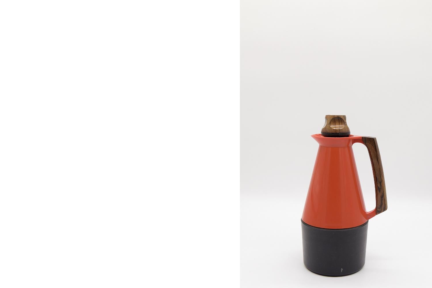 This TV-Kanna Signatur thermos was designed in 1962 by Carl-Arne Breger for the Swedish manufacturer Husqvarna Borstfabrik. A thermos is made of orange-red plastic with a black bottom. The handle and lid are made of solid teak. The inlet is designed