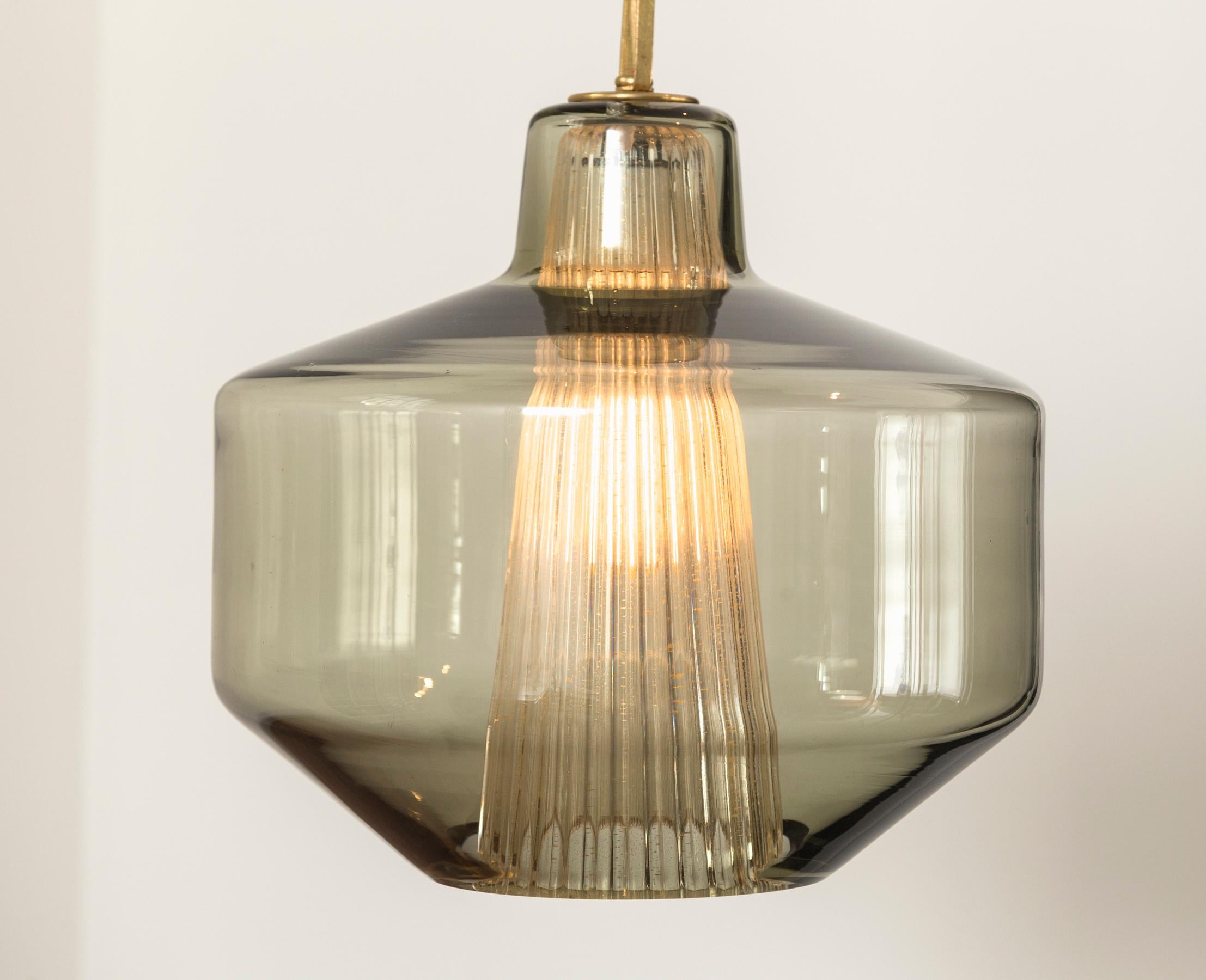 Scandinavian Modern greige glasssphere shaped pendant with interior ribbed cone-shaped glass in clear and gold.

Attributed Designer: Carl Fagerlund for Orrefors

Newly wired porcelain medium base fixture and install ready with unlacquered brass