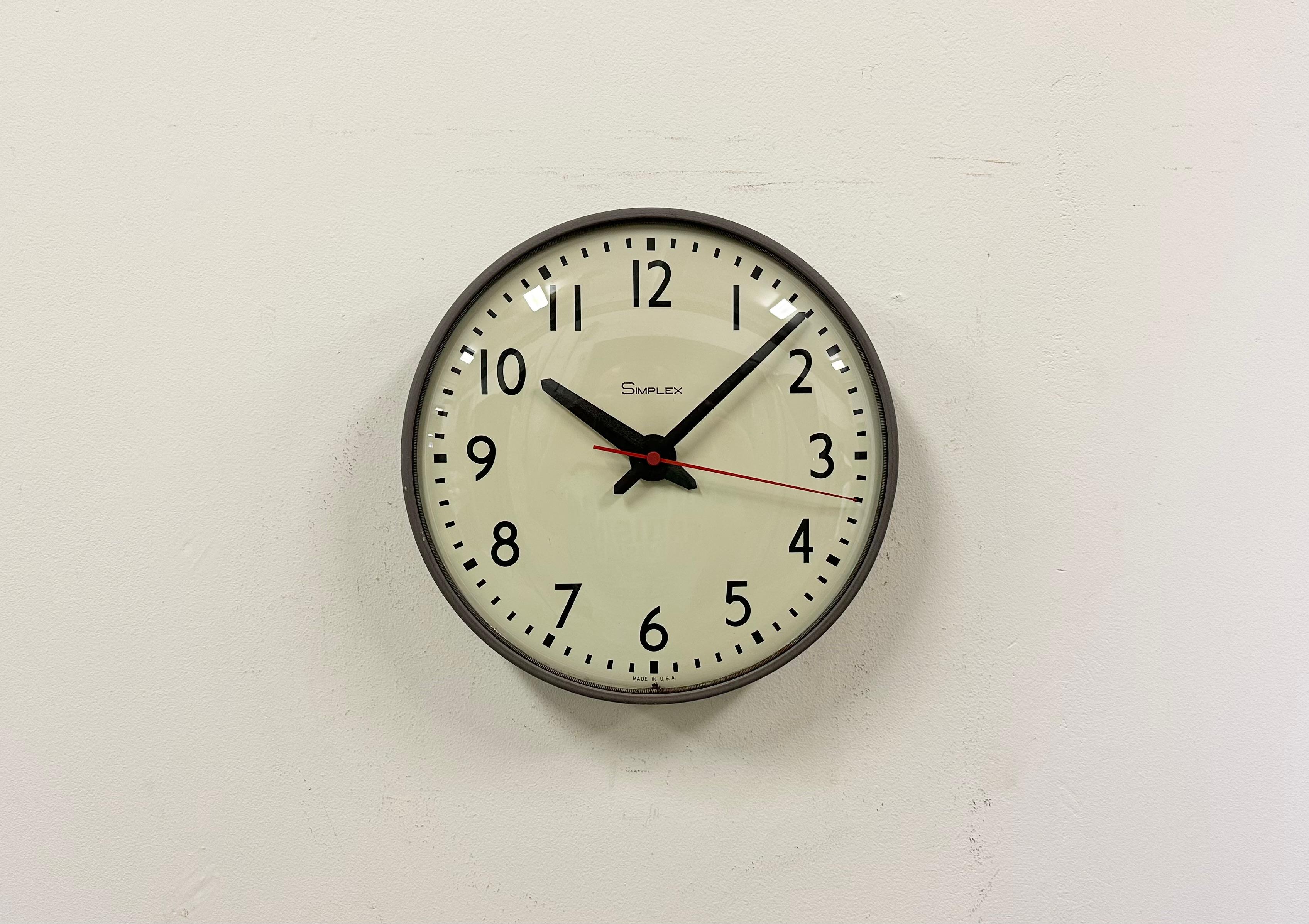 Wall clock made by Simplex Time Recorder Co. in U.S.A. during the 1970s-1980s. It features a grey iron frame, a metal dial, an aluminium hands and curved clear glass cover. The piece has been converted into a battery-powered clockwork and requires