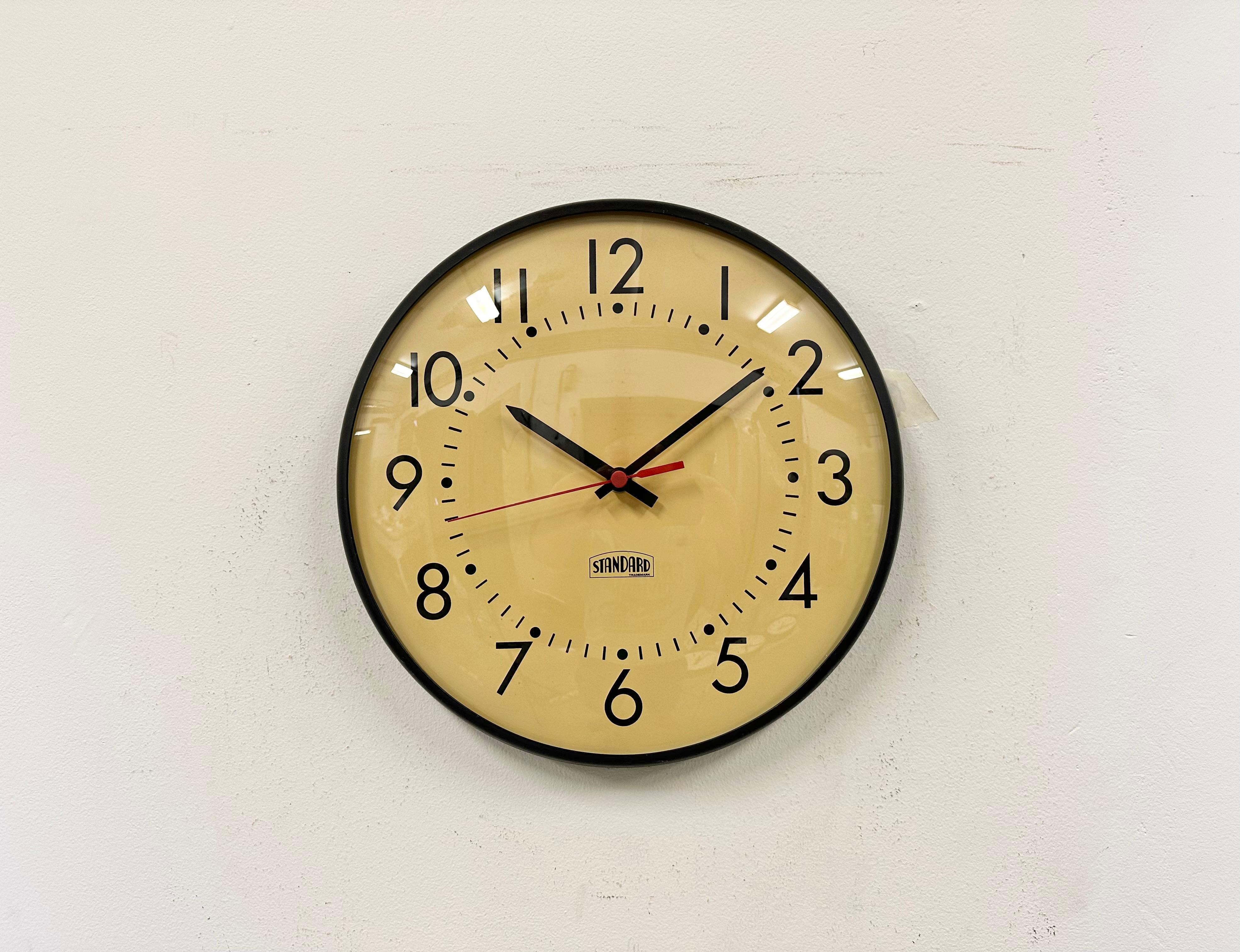 Wall clock made by Standard Electric in U.S.A. during the 1970s. It features a black iron frame, a metal dial, an aluminium hands and curved clear glass cover. The piece has been converted into a battery-powered clockwork and requires only one