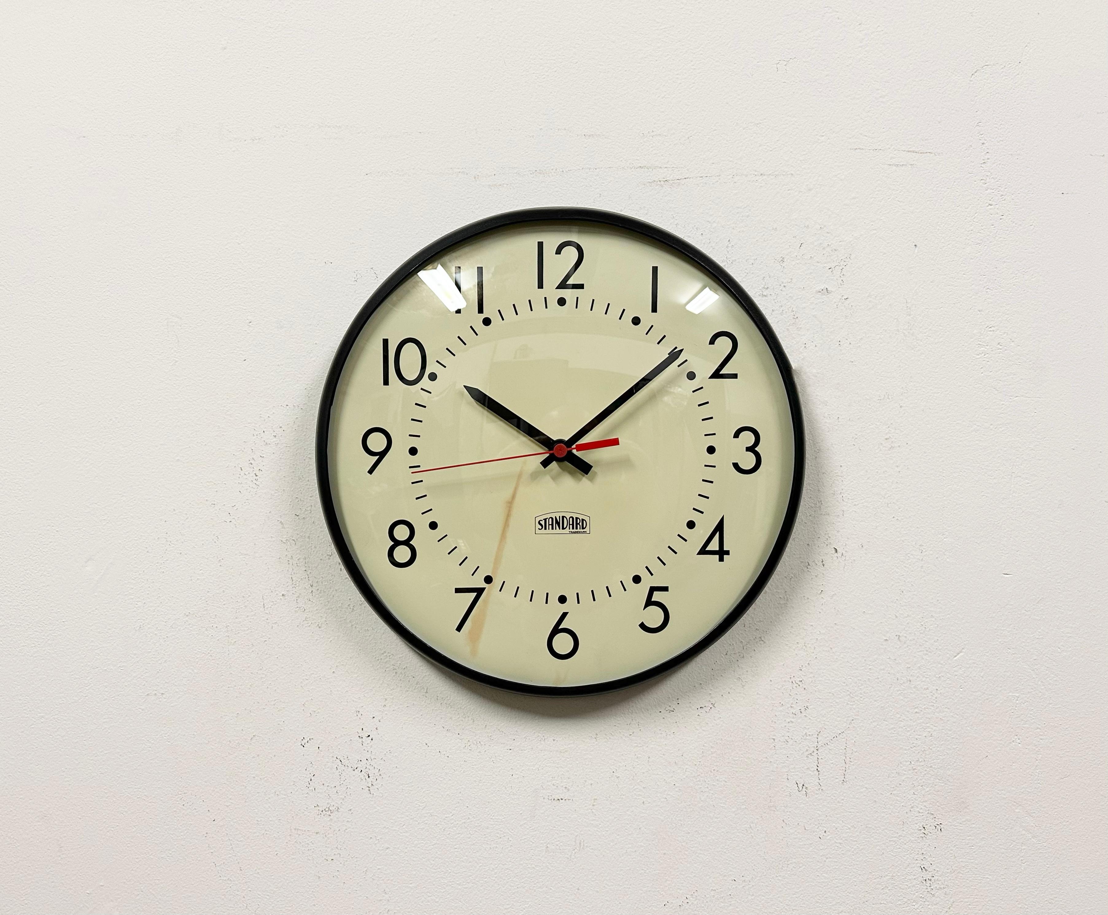 Wall clock made by Standard Electric in U.S.A. during the 1970s-1980s. It features a black iron frame, a metal dial, an aluminium hands and curved clear glass cover. The piece has been converted into a battery-powered clockwork and requires only one
