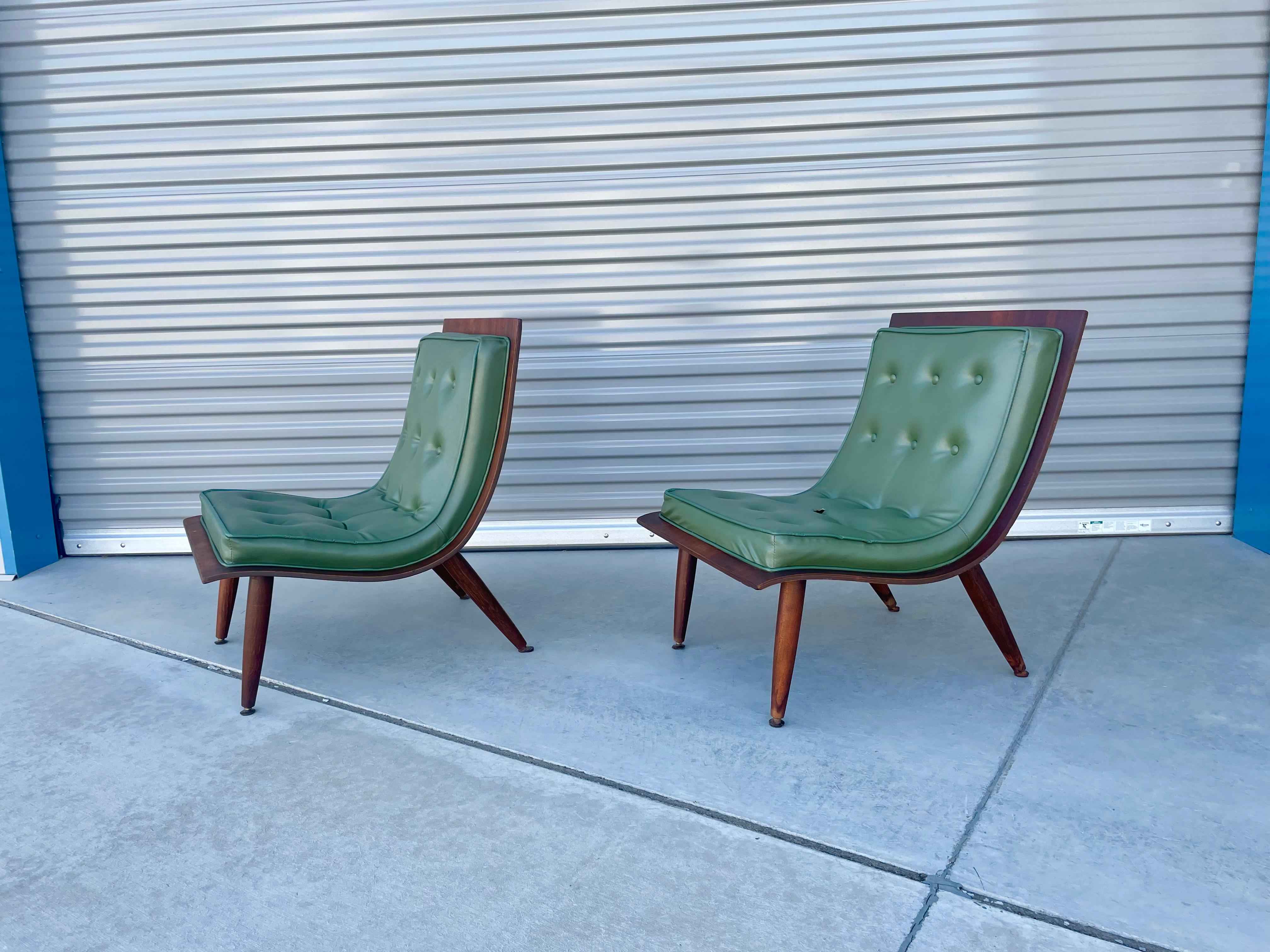 Vintage scoop lounge chairs manufactured by Carter Brothers, circa the 1950s. This mid-century pair of scoop chairs feature a sleek design covered in tufted green leather upholstery with a walnut back. The chairs also have a unique wave shape design
