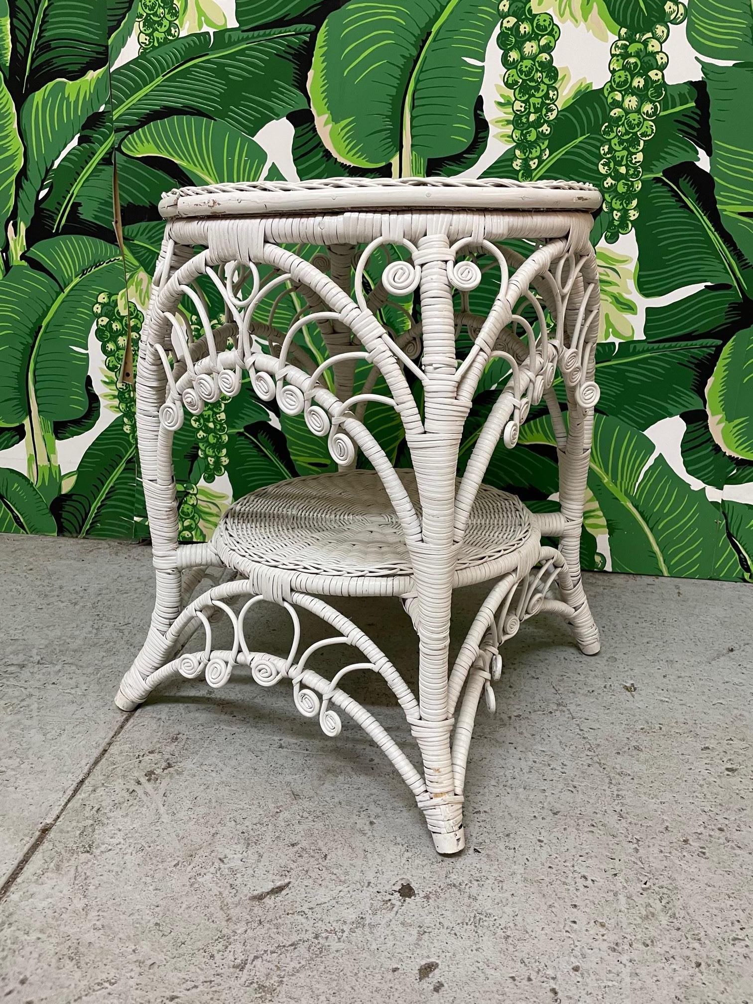 Vintage wicker side or end table features woven top and ornate scrolled and filigree aprons. Rattan wrapped frame and splayed legs. In the manner of Heywood-Wakefield. Good condition with minor imperfections consistent with age.
