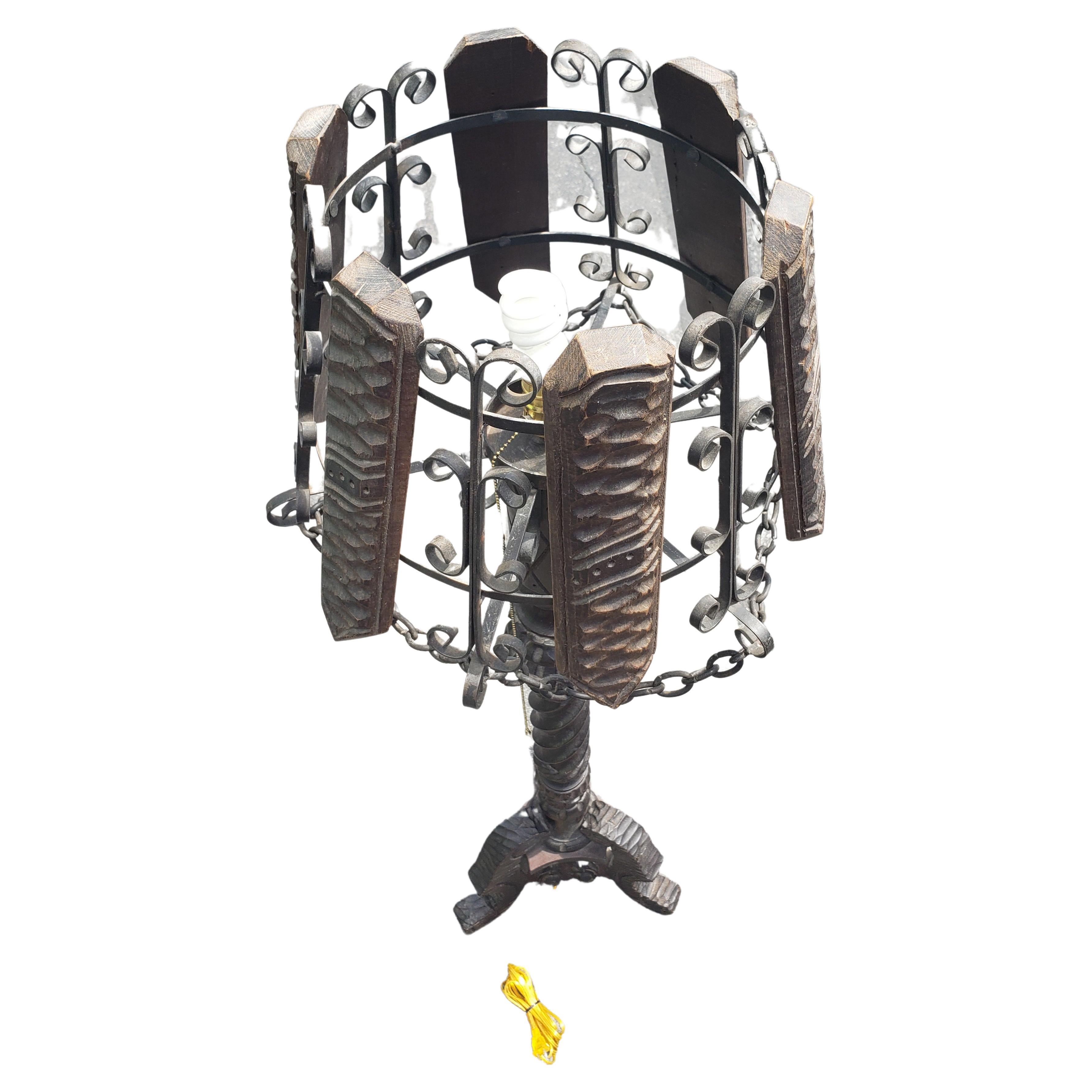 Un lampadaire à piédestal en bois sculpté vintage unique, de style Arts et Artisanat. La colonne sculptée et ébénisée est soutenue par des pieds tripodes. Lamelles en bois et abat-jour en fer agrémentés d'une chaîne de suspension. L'abat-jour est