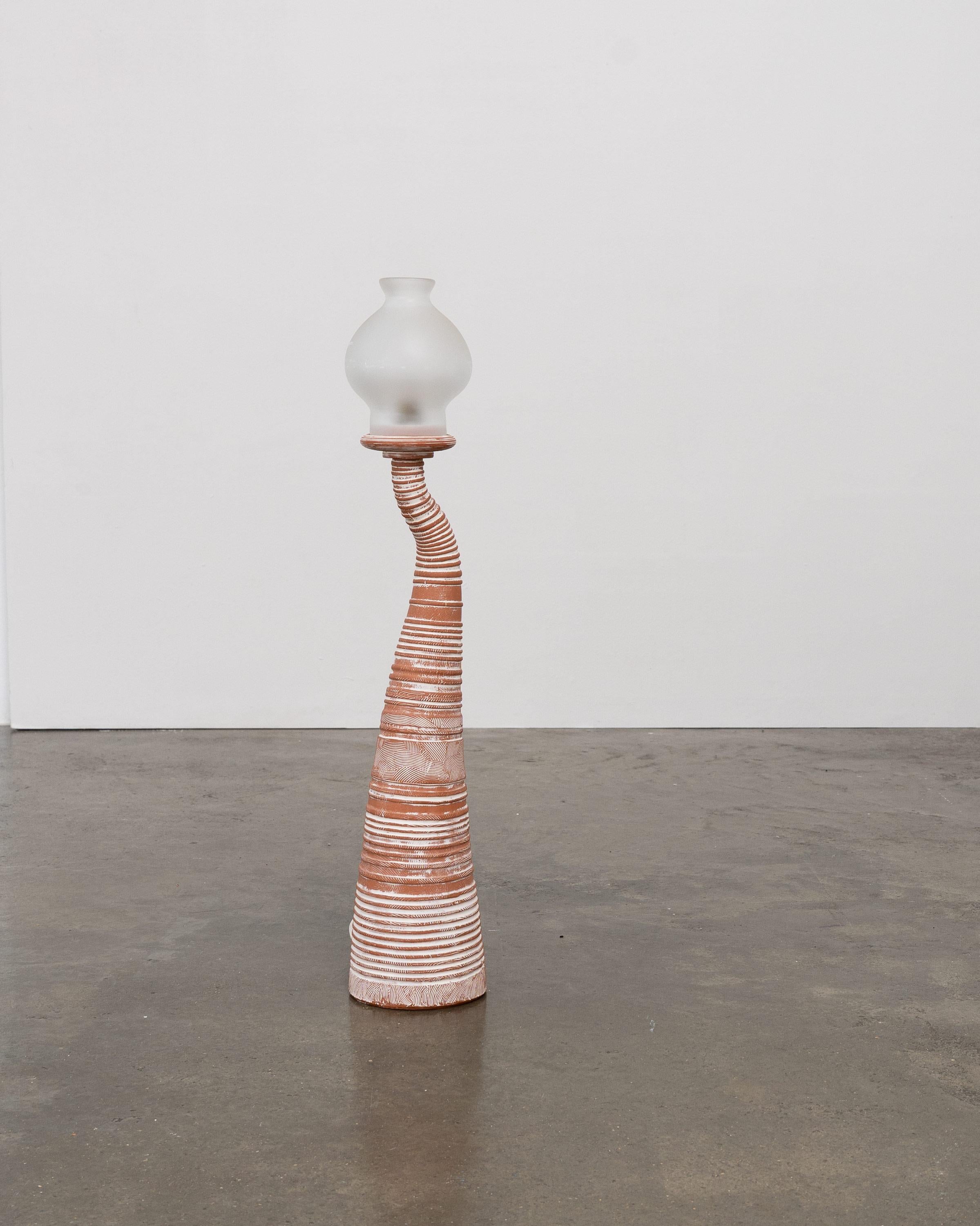 An unattributed studio pottery lamp with a sculptural handmade terracotta base featuring textured impressions highlighted with a white underglaze. The base is accompanied by a removable frosted glass shade. 

This is the shorter of two lamps