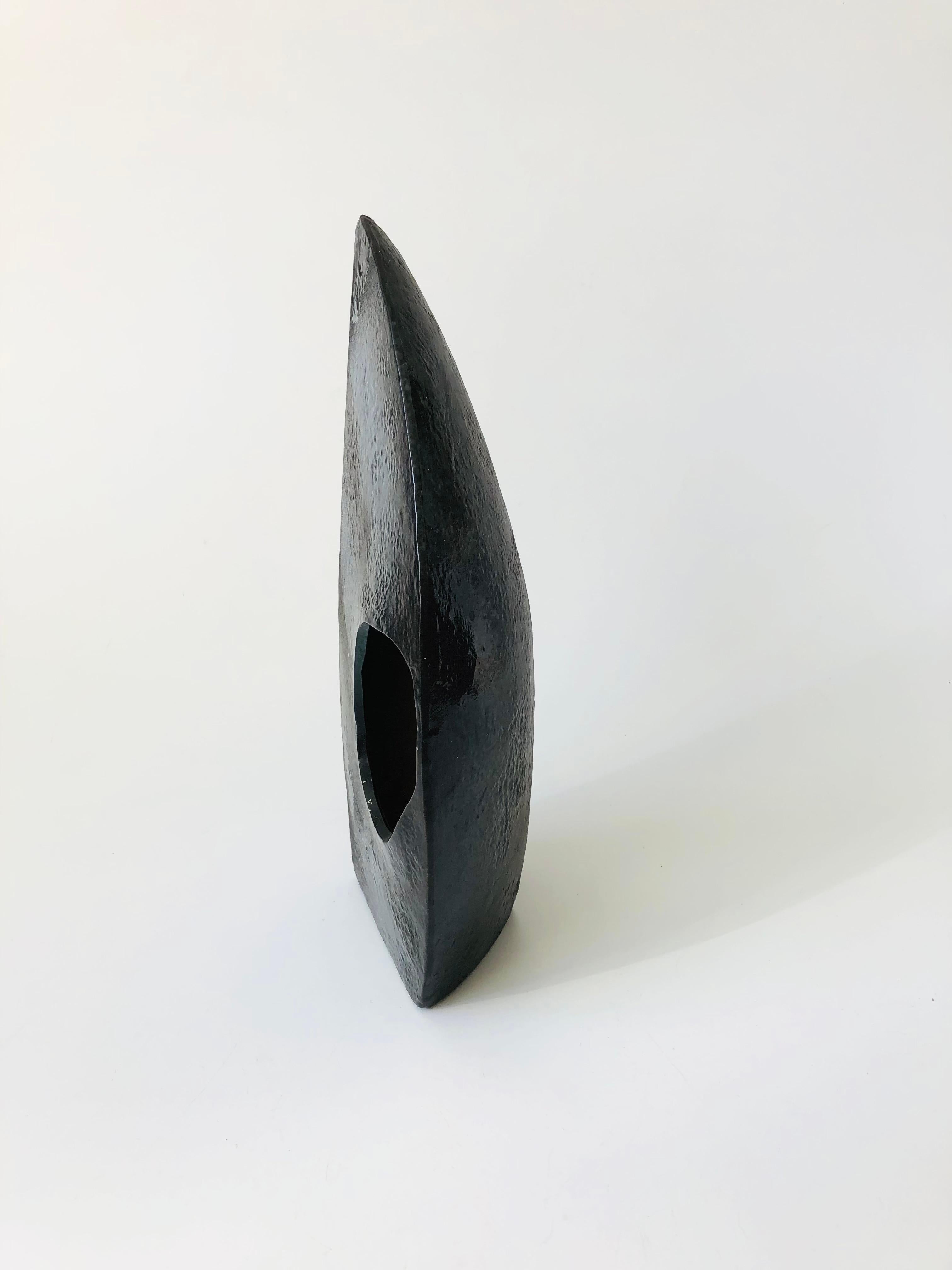 A vintage sculptural pottery ikebana vase. Dramatic dark glaze with wonderful variation and light texture. In a crescent moon shape with an offset circular opening. Can be displayed upright or flat on a table top.

