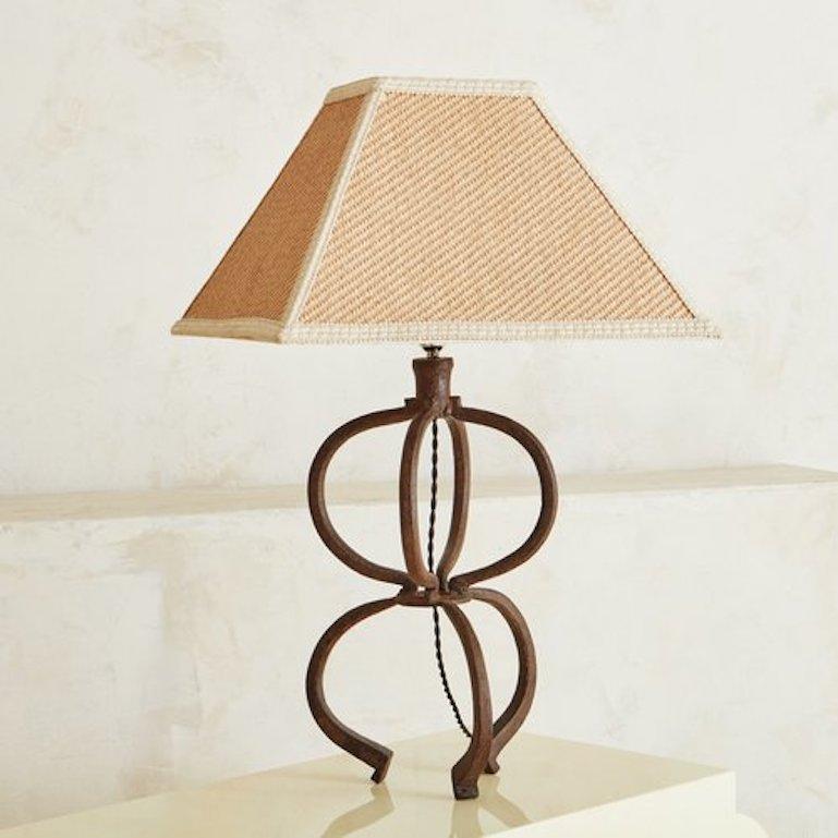 A sculptural table lamp featuring a curved iron body. This lamp has a woven, rectangular shade with cream piping. Sourced in Spain, 1970s. 

