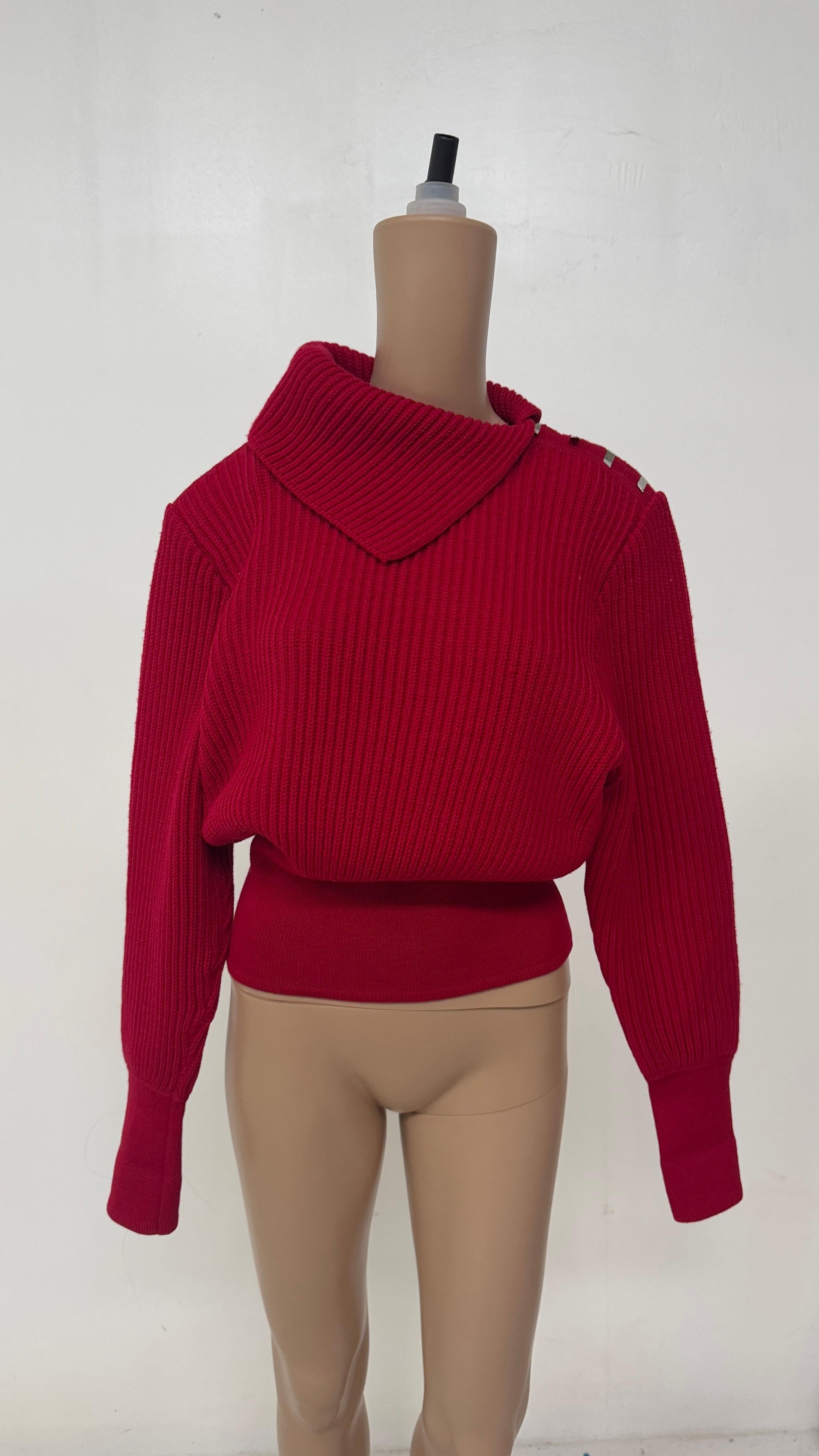 Ce pull vintage saisissant est fabriqué en pure laine rouge riche et présente une silhouette sculpturale unique avec une haute encolure en entonnoir et un tricot côtelé exagéré. Ce qui distingue vraiment cette pièce, c'est le détail innovant de