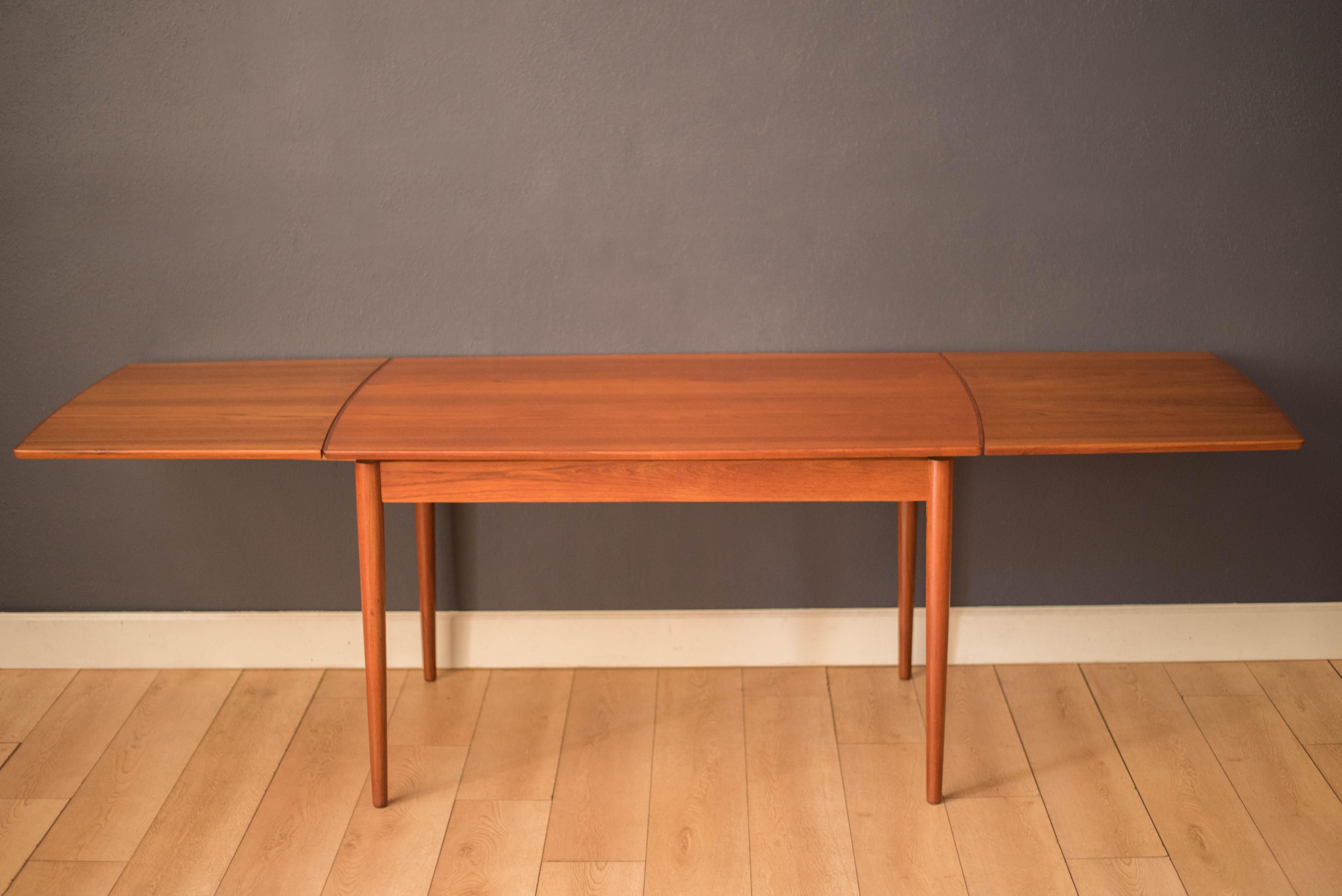 Table de salle à manger à tiroirs en teck, circa 1960. Ce plateau de table unique en forme de bateau présente des grains continus et fluides encadrés par des bords incurvés en teck massif. Soutenu par des pieds classiques en forme de crayon effilé,