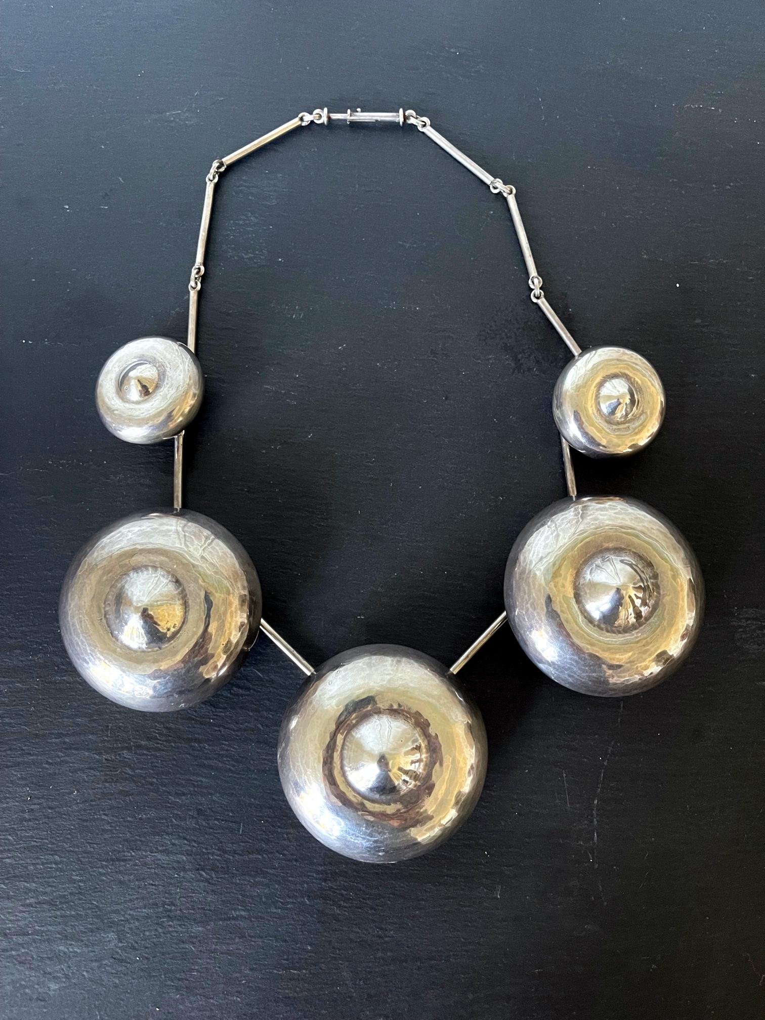 A bespoken sterling silver necklace with five roundel bell shape of gradual sizes linked by joint chains, designed and made by Graziella Laffi, Lima, Peru, circa 1965. The subtly hammered roundels evoke a sense of history with the form found in