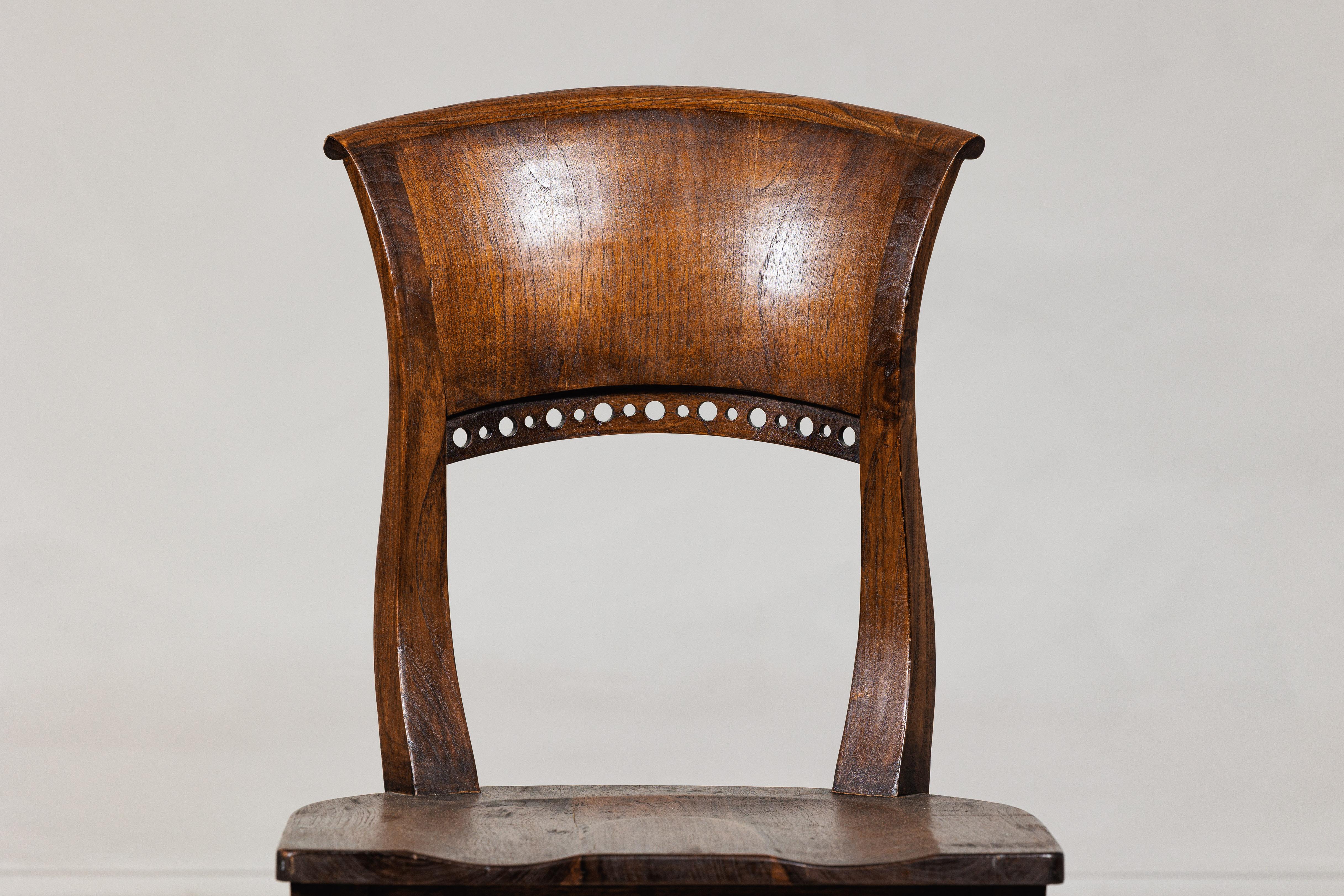 This vintage side chair showcases sculptural craftsmanship with a strong silhouette and subtle detailing. The elegantly curved backrest fans outward in a broad flare, adding visual movement and comfort. A row of round piercings just below the