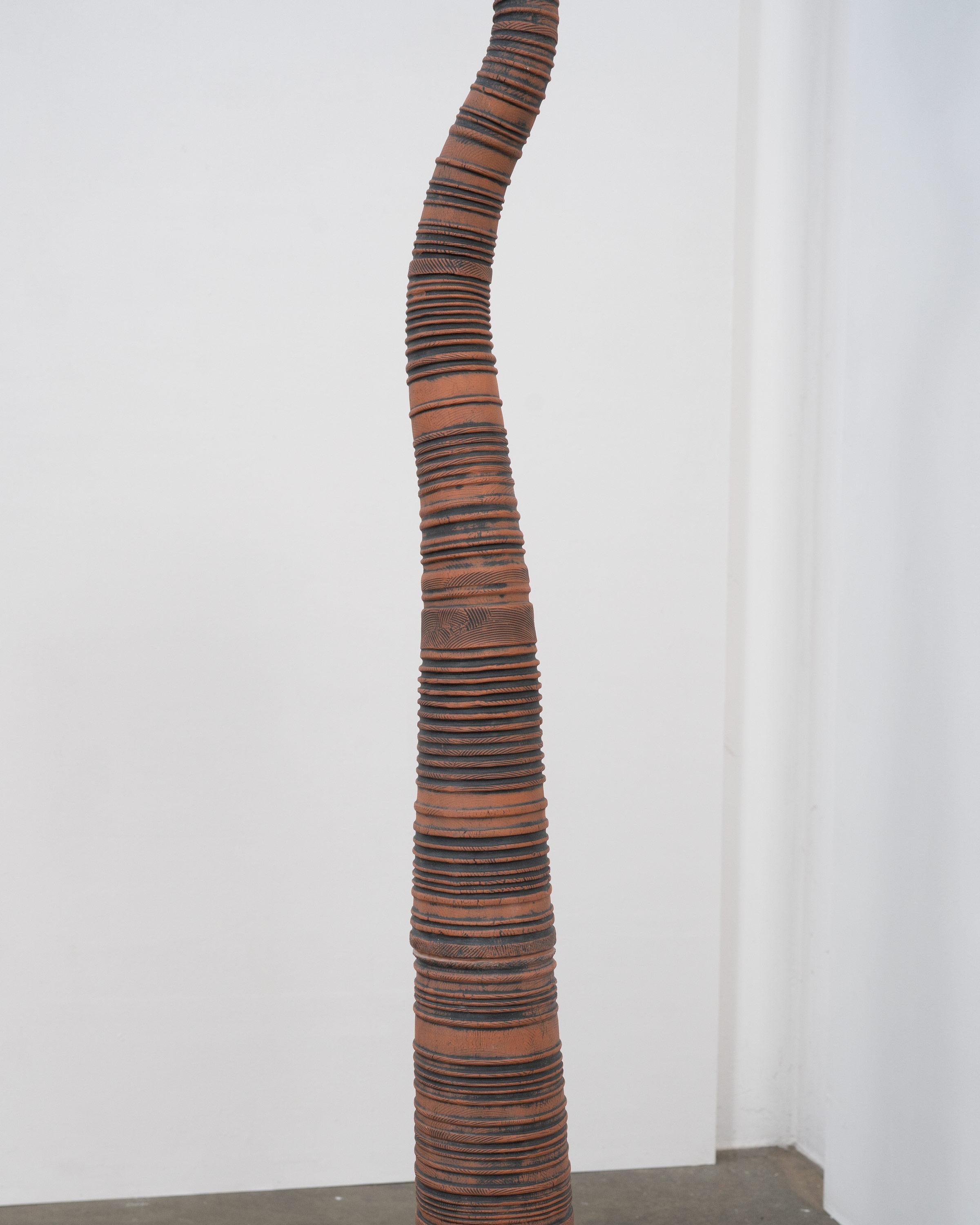 An unattributed studio pottery floor lamp with a sculptural handmade terracotta base featuring textured impressions highlighted with a black iron oxide wash. The base is accompanied by a removable frosted glass shade. 

This is the taller of two
