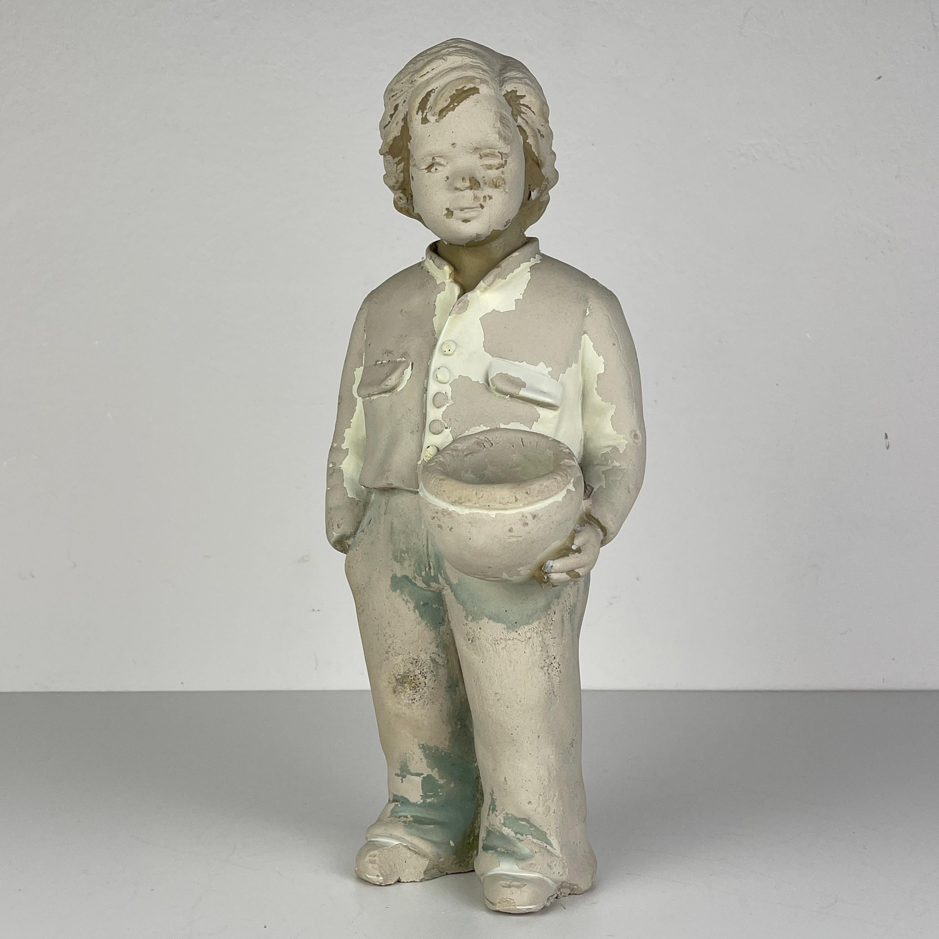 Introduce a touch of vintage charm to your space with this Yugoslavian Boy Sculpture from the 1960s. Crafted from plaster, this petite figurine stands at a height of 36 cm, capturing the essence of mid-century artistry. Despite its vintage allure,