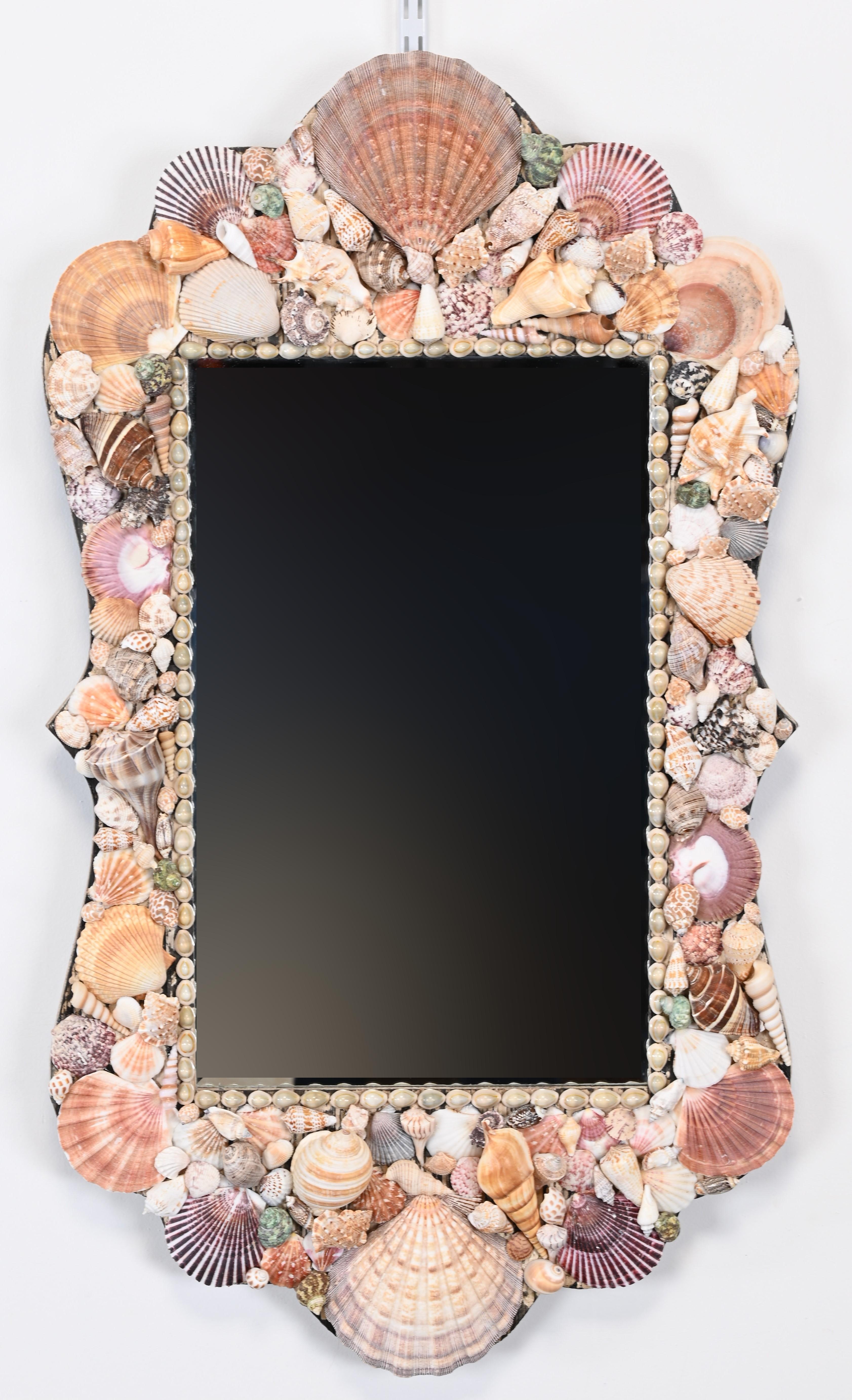 A beautiful seashell mirror in the manner of Anthony Redmile, London. This beveled glass mirror would look great in a hallway, over a mantle, in a bathroom, or powder room. Perfect for a beach house, cottage, or coastal home. Structurally sound and