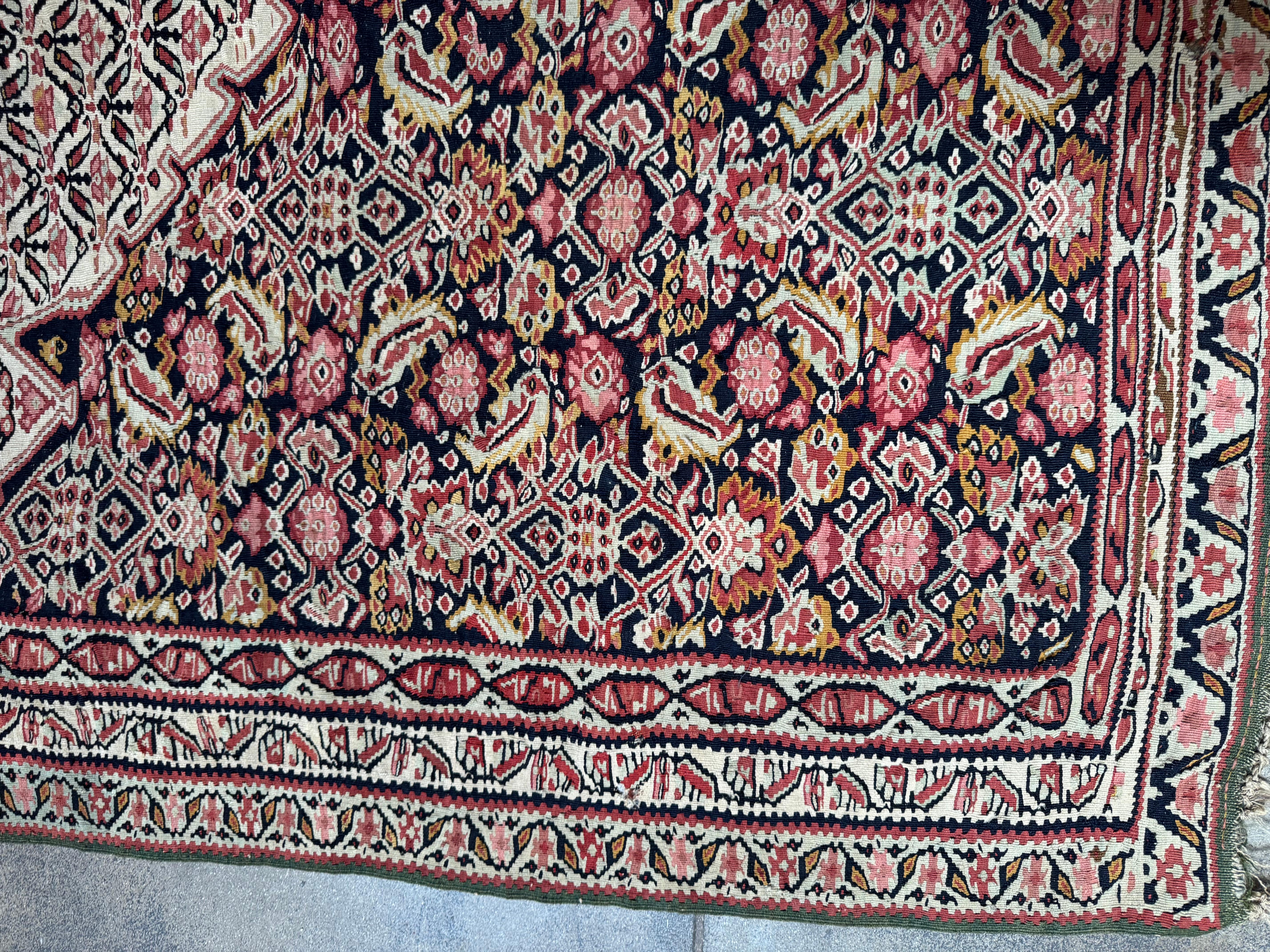 Dieser elegante Seneh-Kilim-Teppich im Vintage-Stil zeigt die raffinierte Handwerkskunst der persischen Stammesweber mit einem komplizierten floralen Rautenfeld und einem atemberaubenden Medaillon in der Mitte. Das Design in tiefen Marine-, Rosé-,