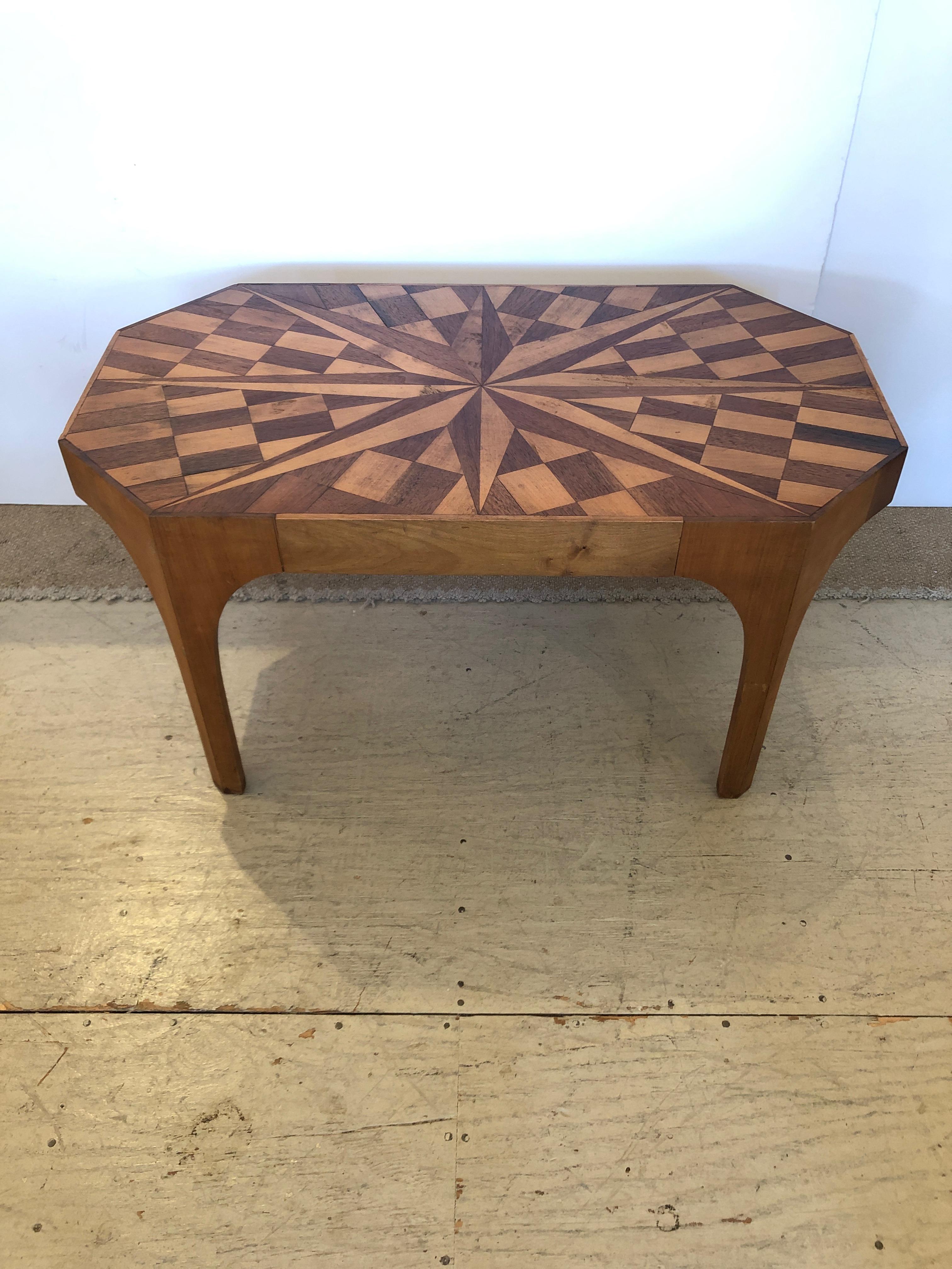 A stunning medium sized vintage coffee table having gorgeously crafted mahogany and walnut inlay with central starburst design surrounded by geometric checkerboard pattern. The shape is a rectangle with angled corners to make 8 sides. Great