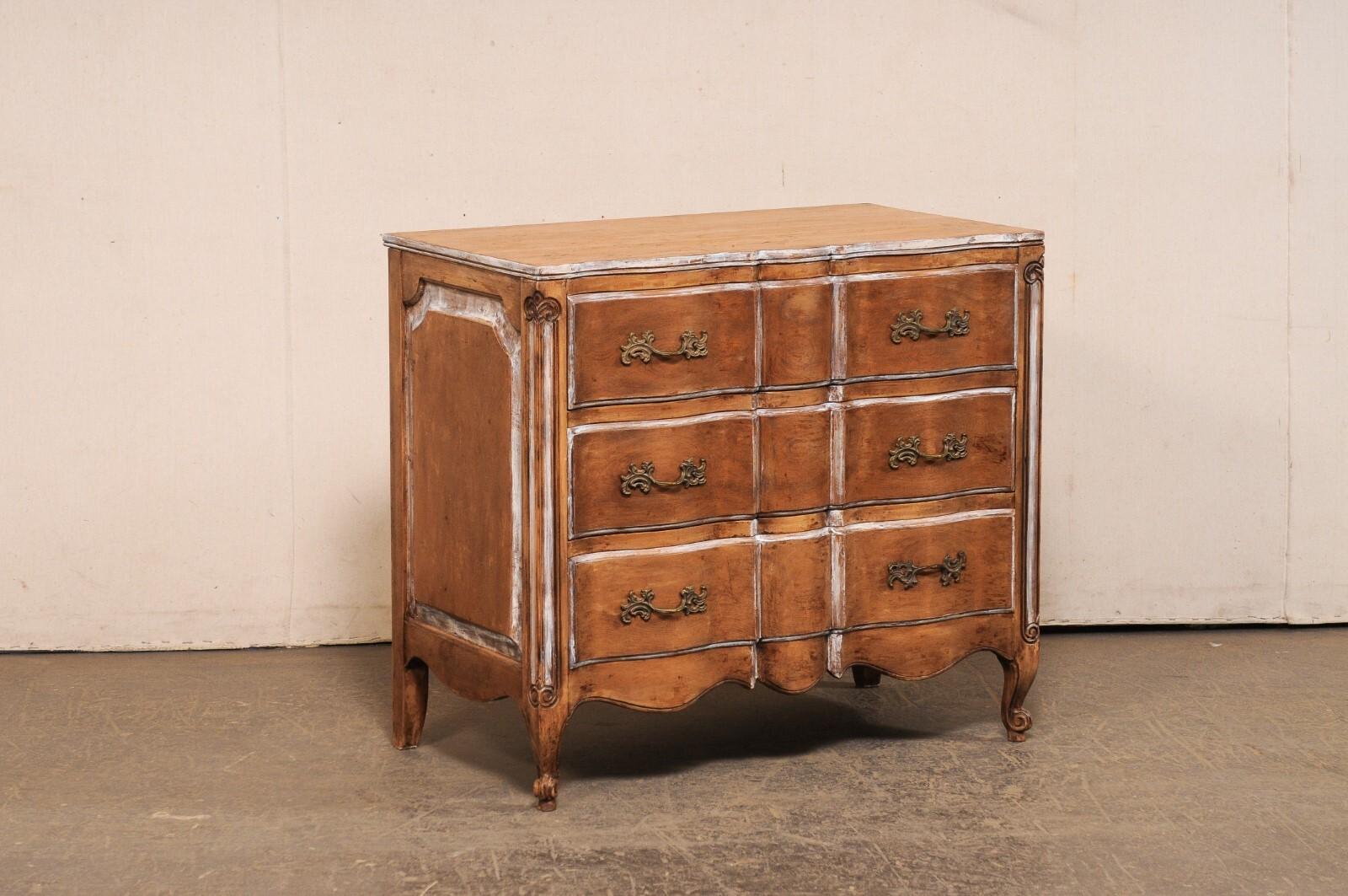 A French-style carved-wood serpentine commode with three drawers, from the mid 20th century. This mid-century chest, likely American, but designed with French influences, has a serpentine-shaped body, with front top carvings continuing the motif