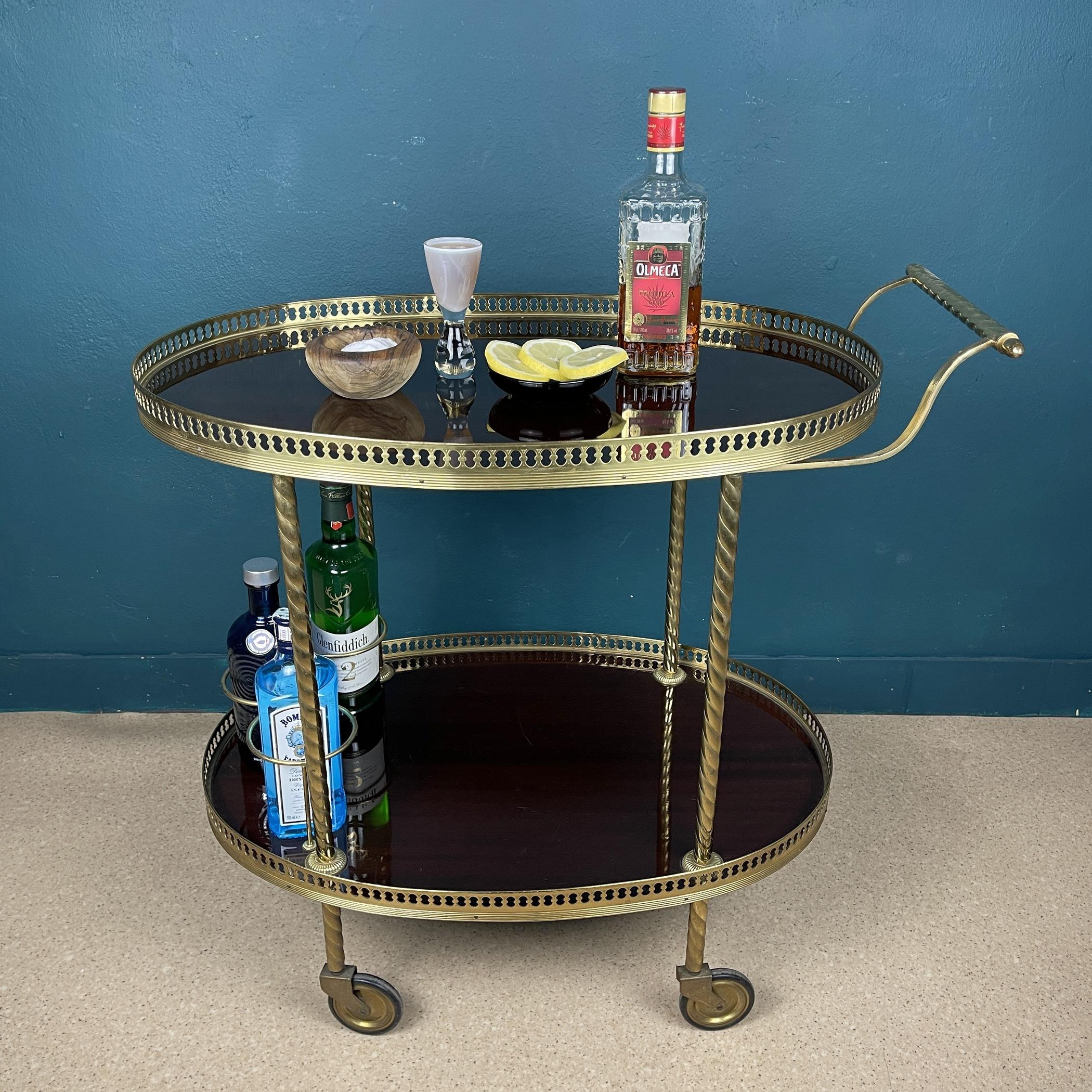 Vintage Italian trolley on 4 wheels. This cocktail bar drinks cart was made in Italy in the 1960s Hollywood Regency style. It has surrounded by a filigree brass railing around an oval tray. Original brass wheels.
The bottom plate has a bottle