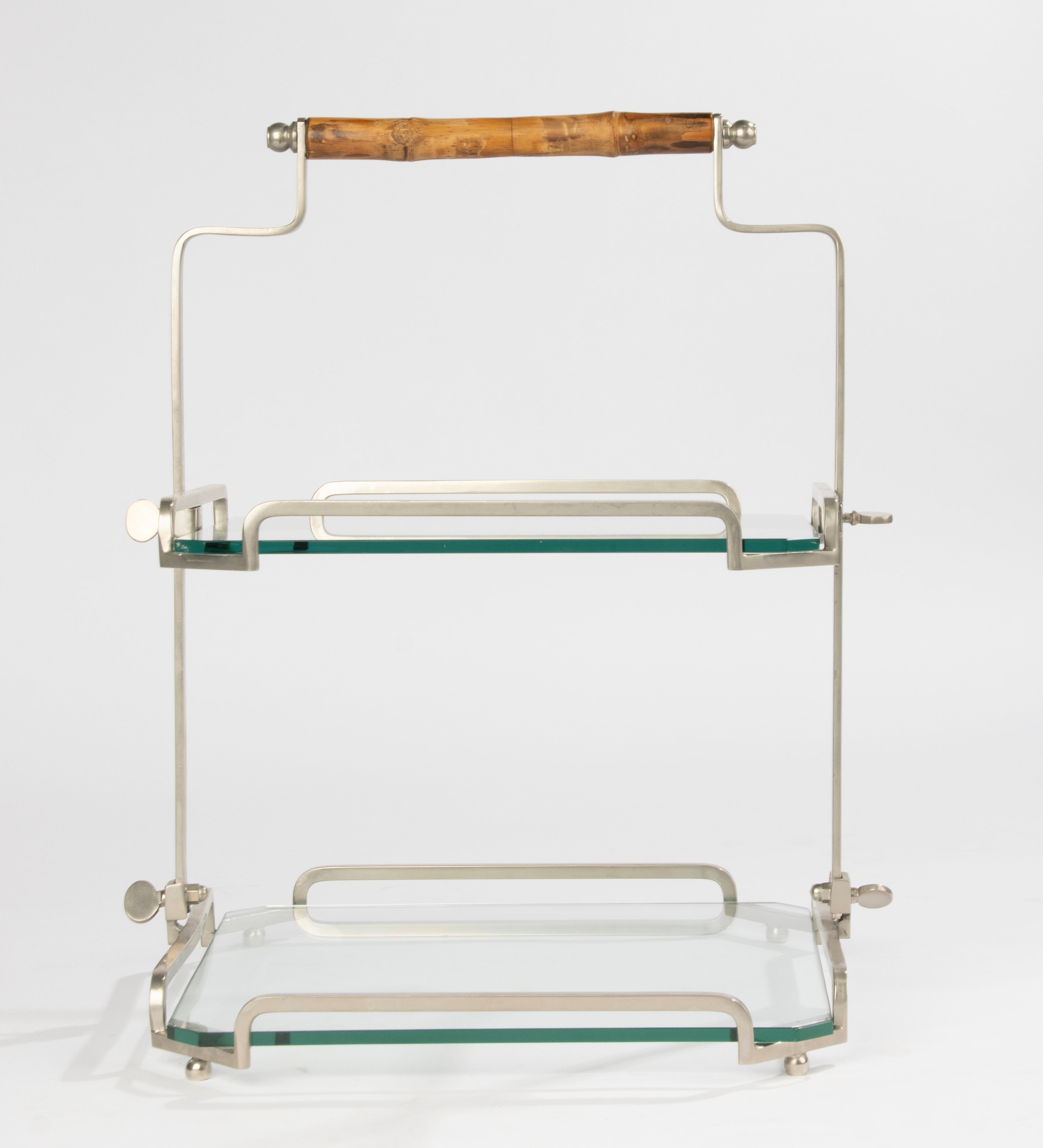 Elegantes zweistöckiges Serviergestell aus den 1960er Jahren. Dieses raffinierte Möbelstück verfügt über einen klaren, vernickelten Metallrahmen, dicke Glasböden mit abgeschrägten Ecken und einen schön gedrechselten Bambusgriff, der einen warmen,